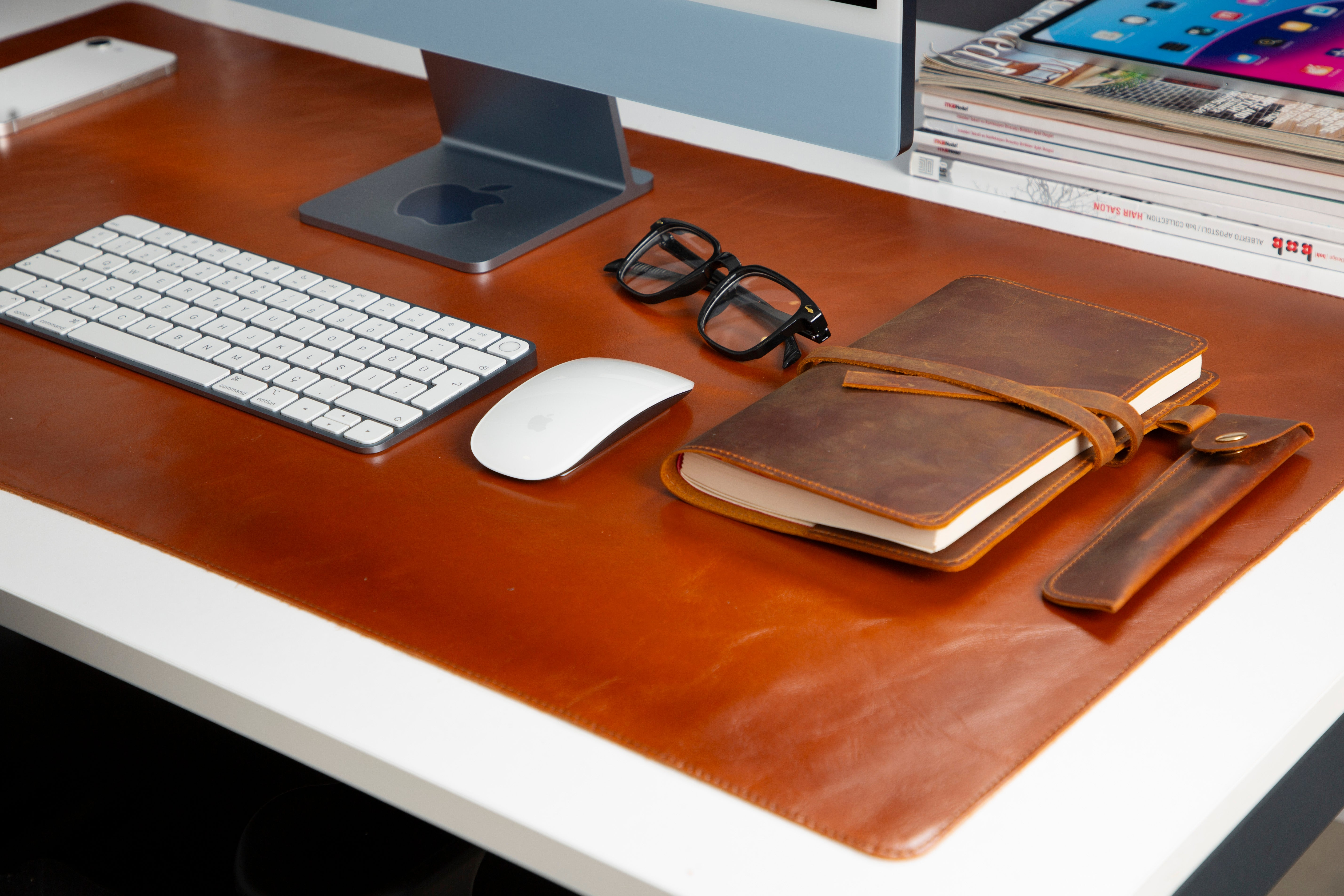 Apple iMac, klavye, fare, gözlük ve defter bulunan bir masa.