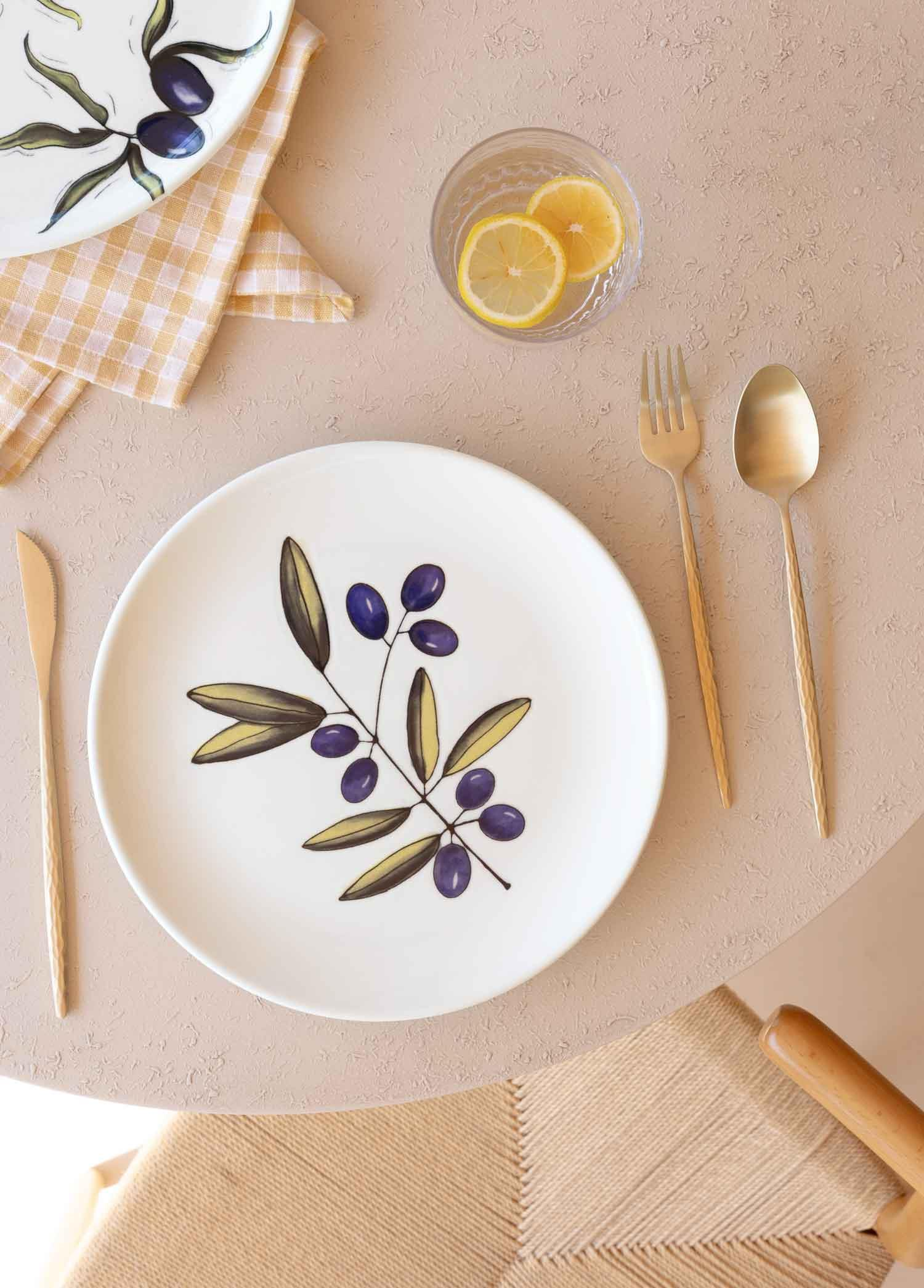 Zeytin dalı desenli tabak, yanında çatal, bıçak ve limonlu su bardağı.