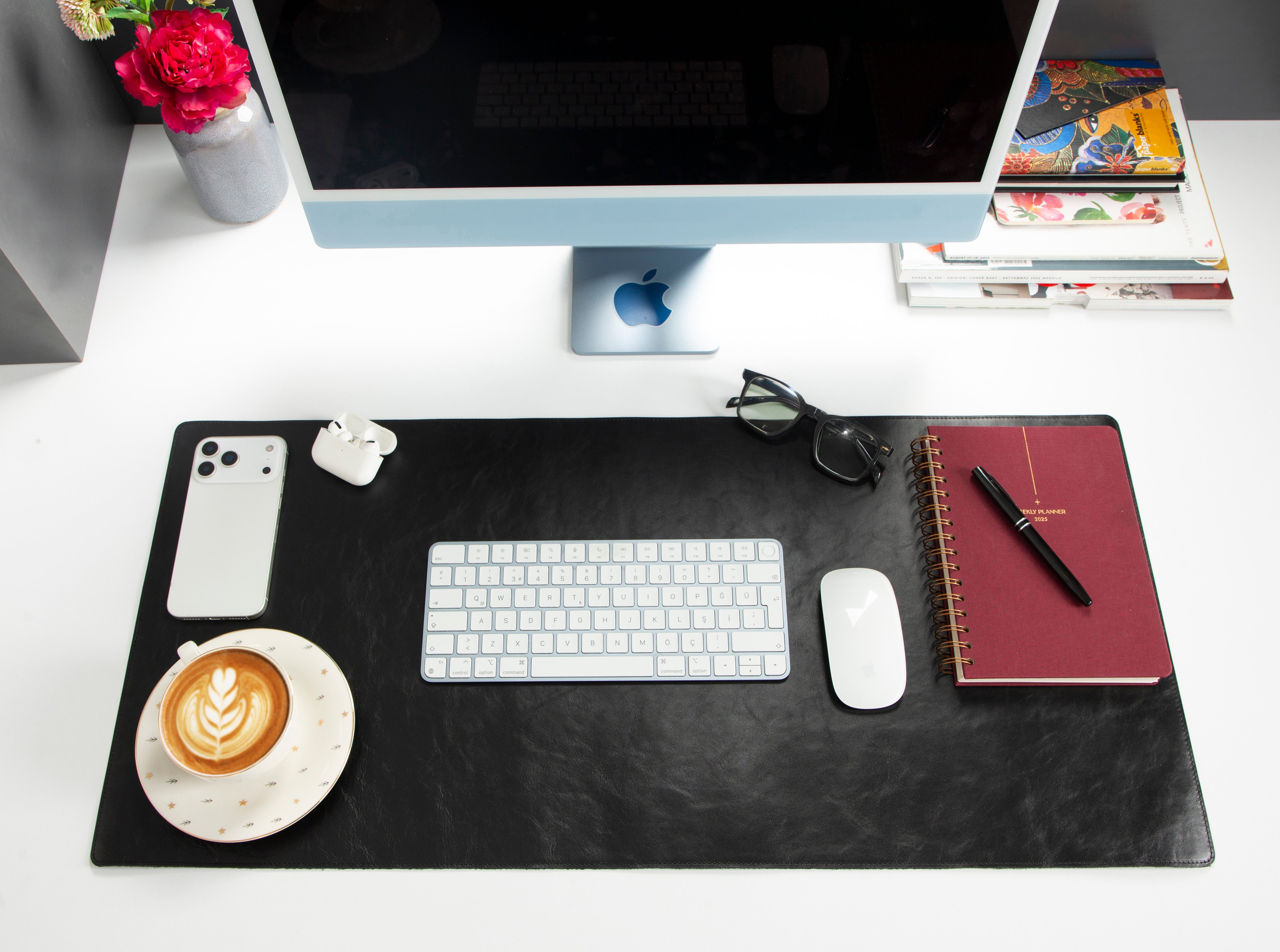 iMac, klavye, fare, telefon, kulaklık, kahve ve defter bulunan bir masa.