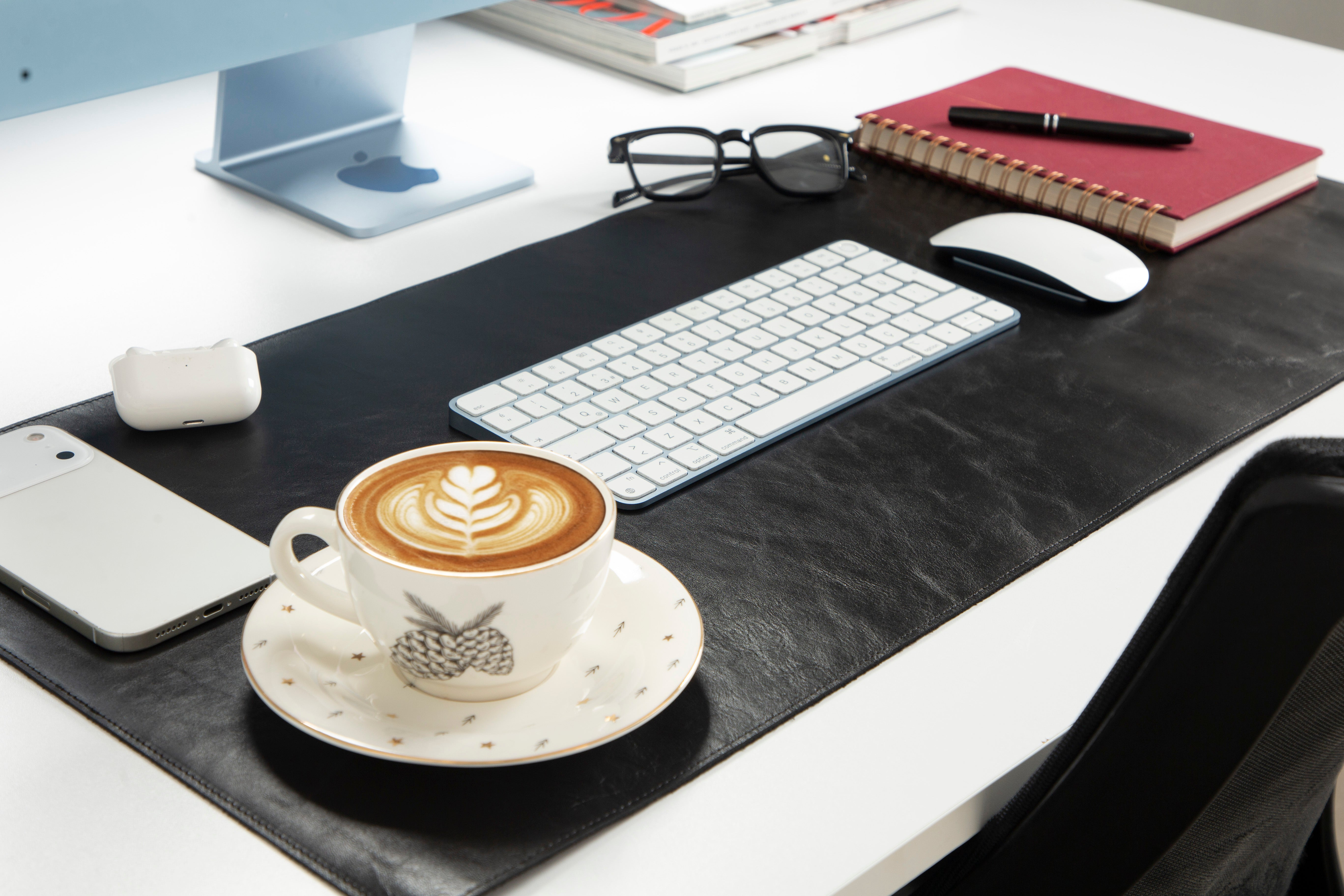 Bir akıllı telefon, klavye ve gözlüğün yanında latte artlı bir kahve fincanı.