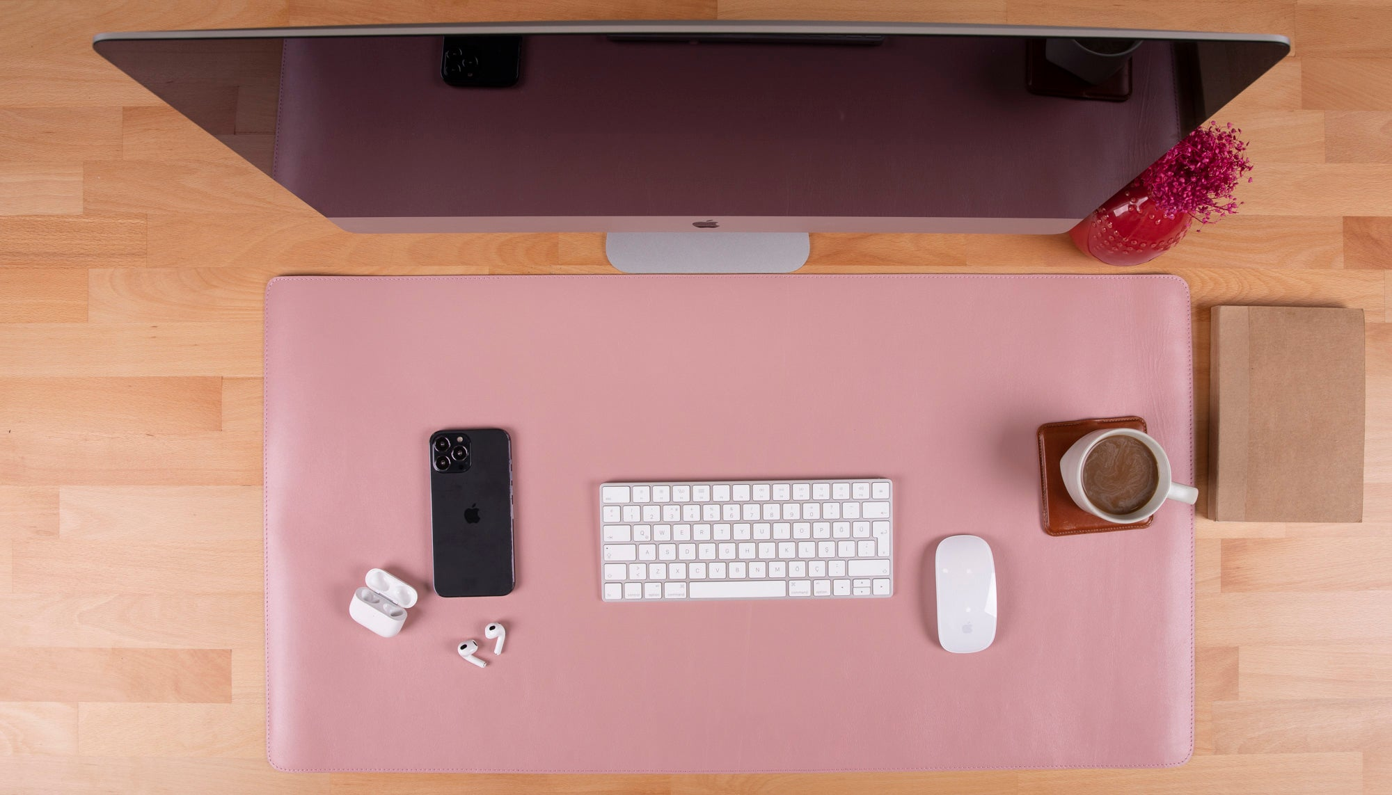iPhone, klavye, fare, kulaklık ve kahve bulunan pembe masa altlığı.