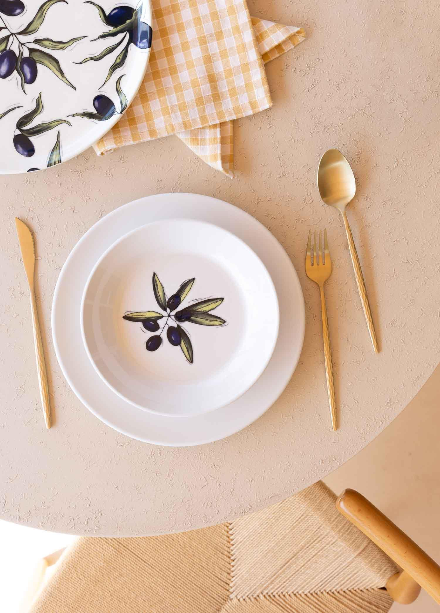 Zeytin motifli bir tabağın yanında masada duran altın rengi çatal bıçak.