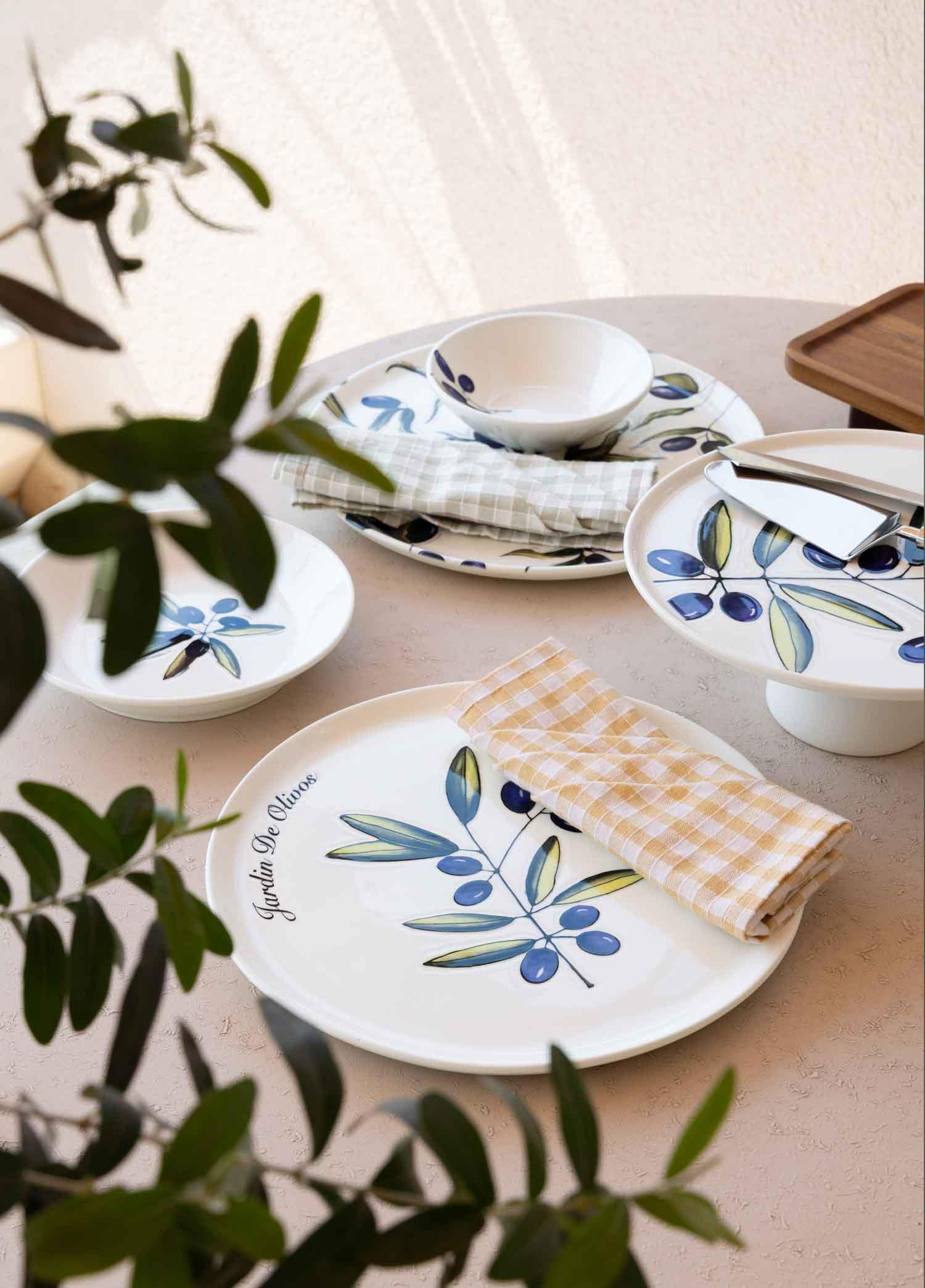 Zeytin dalı desenli beyaz tabaklar ve kareli peçeteler masada.