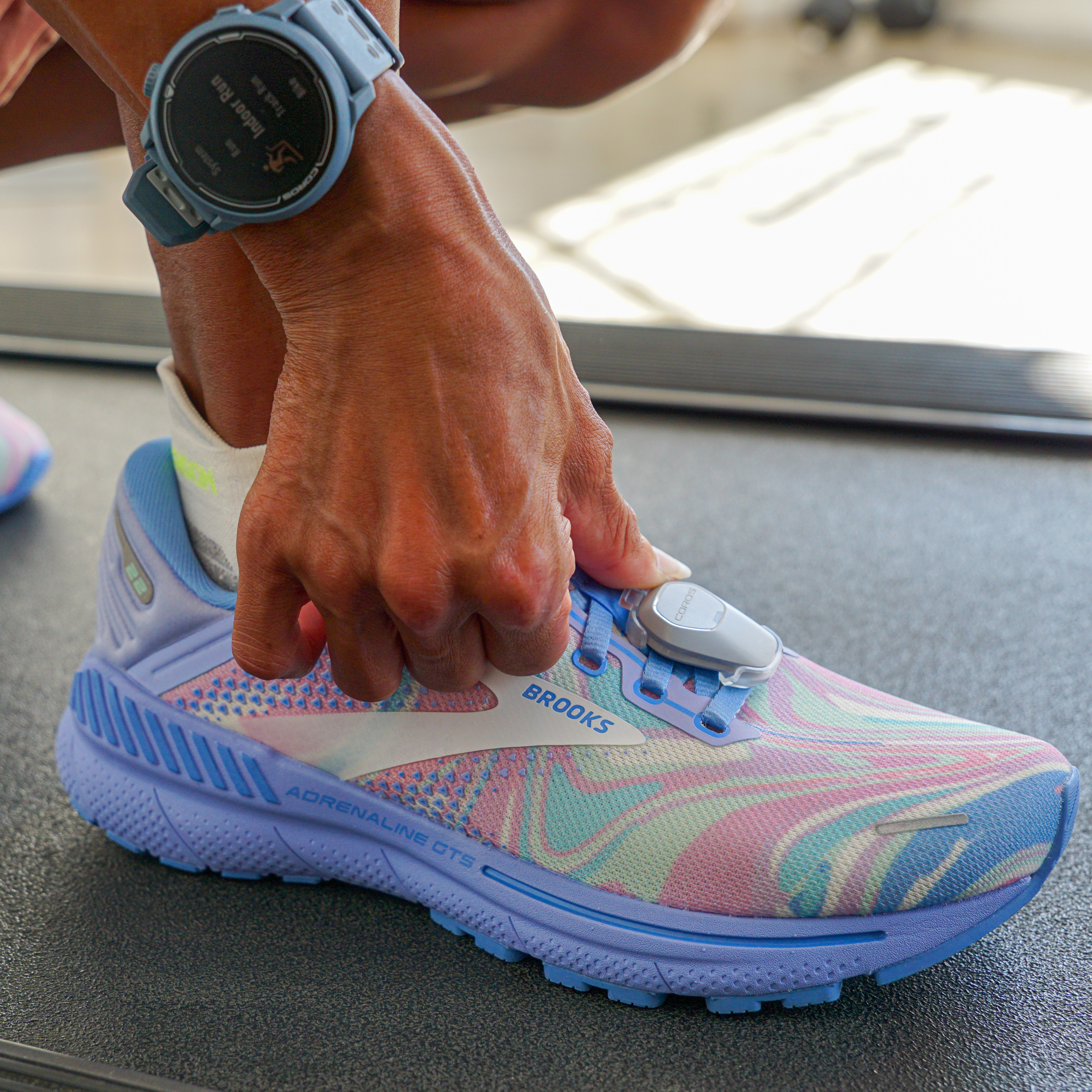 Una mano attacca un sensore a una scarpa da corsa colorata con orologio.