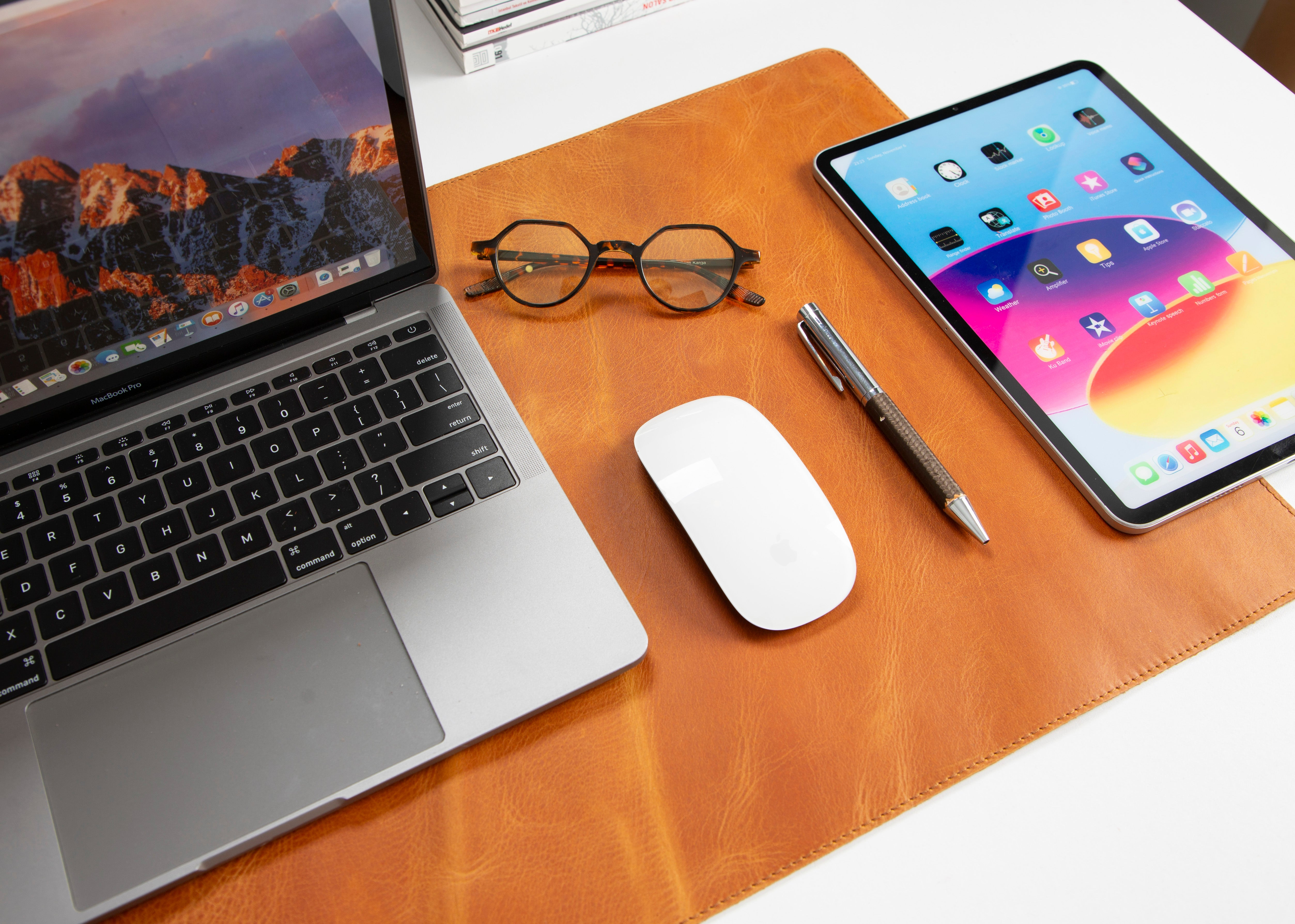 Deri bir mat üzerinde dizüstü bilgisayar, tablet, fare, kalem ve gözlük.