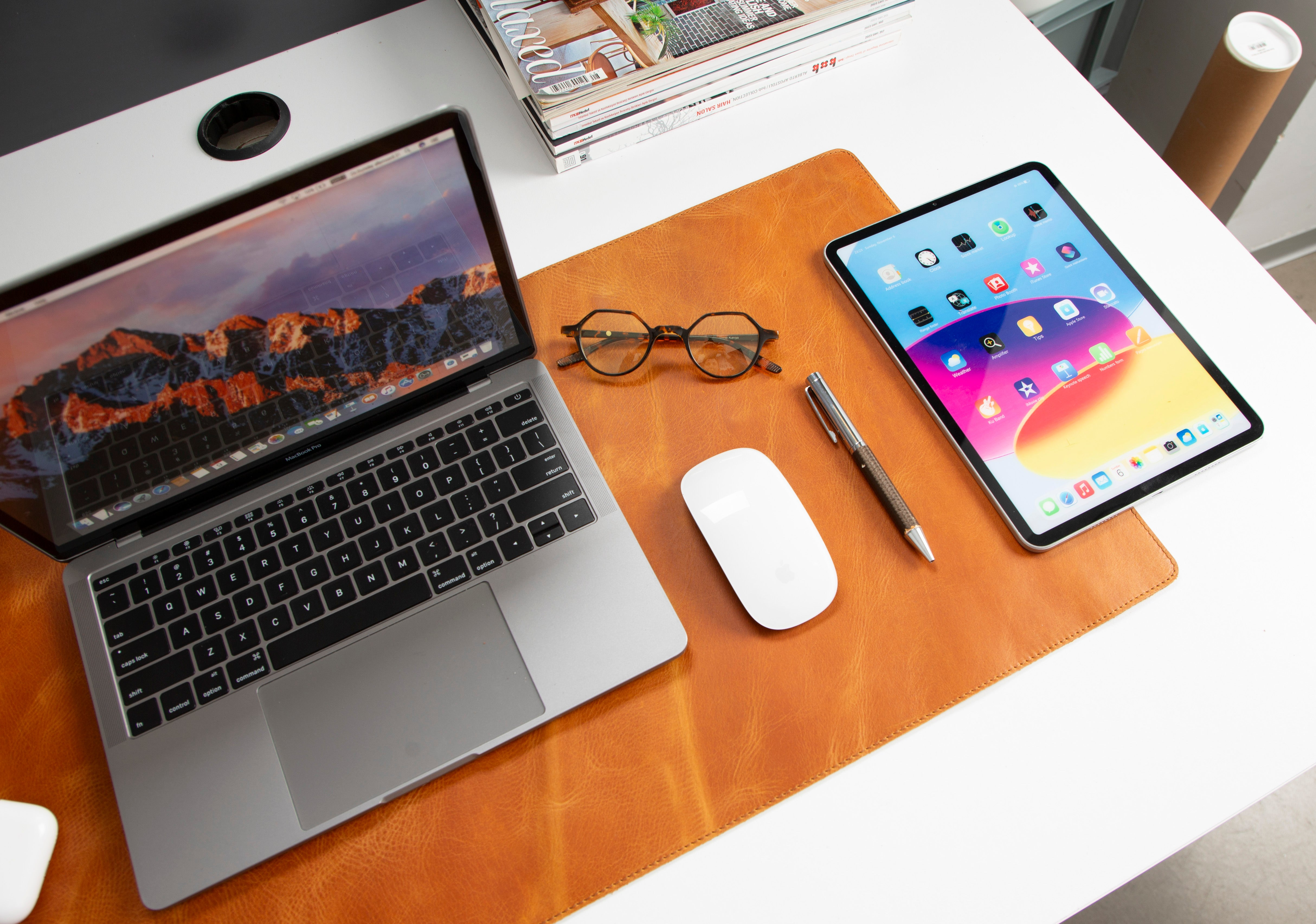 Kahverengi bir mat üzerinde dizüstü bilgisayar, tablet, gözlük, fare ve kalem.