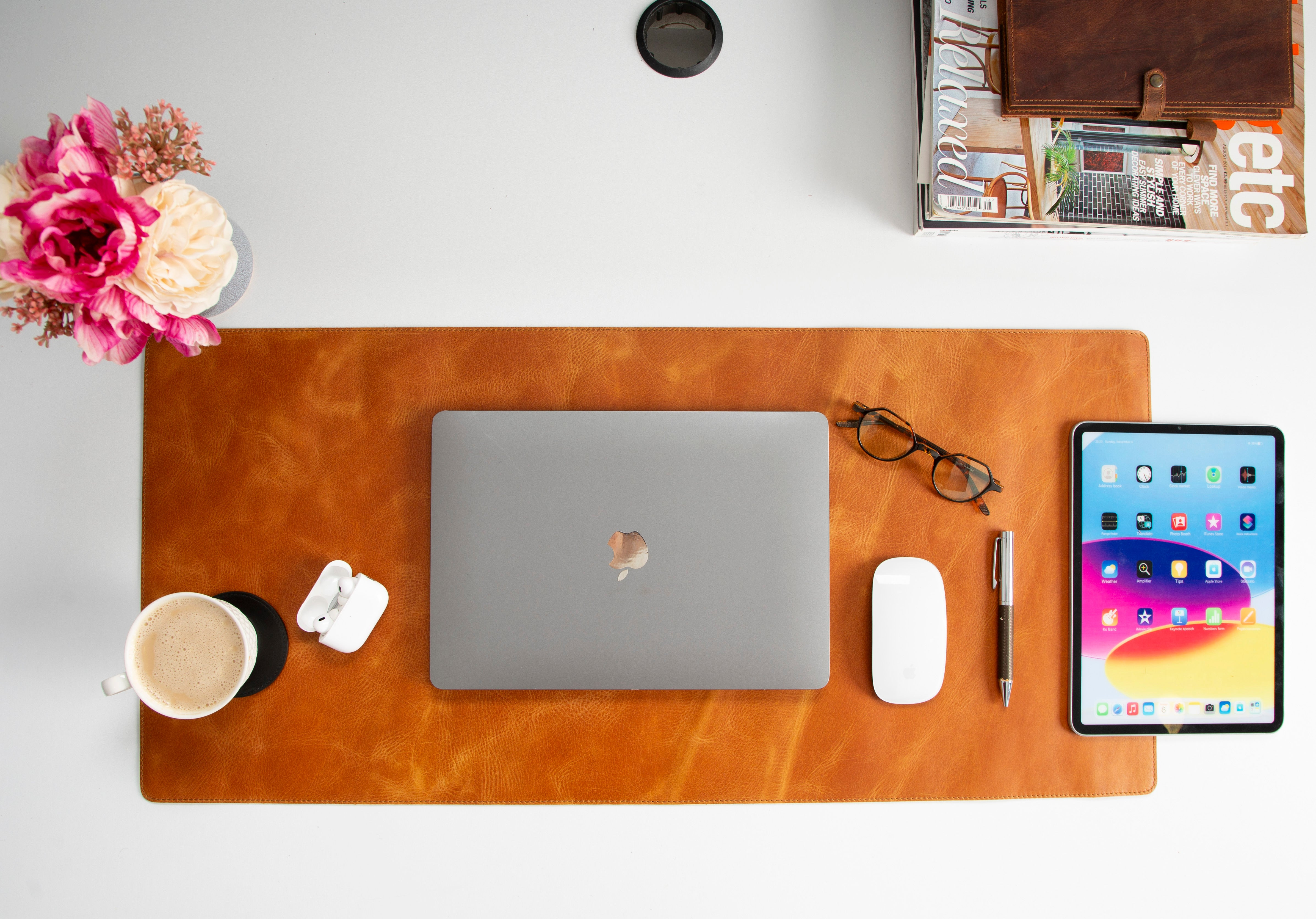 Laptop, tablet, fare, kalem, çiçekler ve kahve fincanı olan masa.