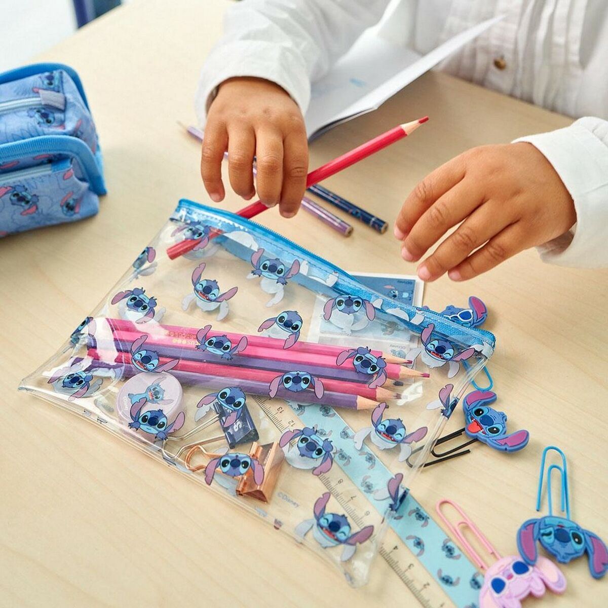 Ein Kind packt Stifte aus einer durchsichtigen Tasche mit Stitch-Motiv aus.