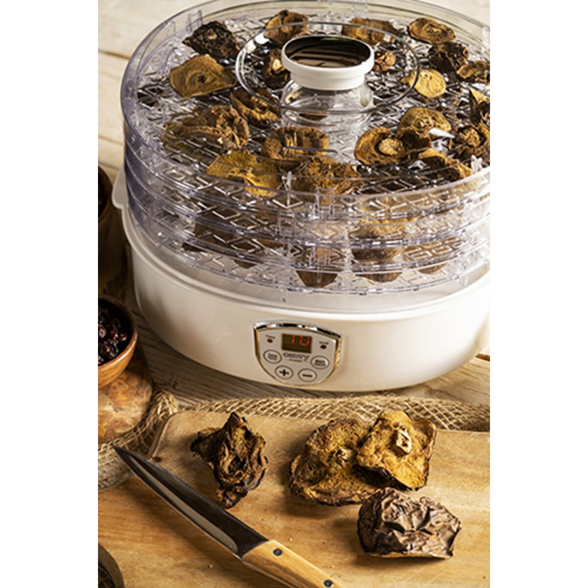 Un essiccatore alimentare a più livelli è riempito di funghi secchi. Legno e coltello in primo piano.