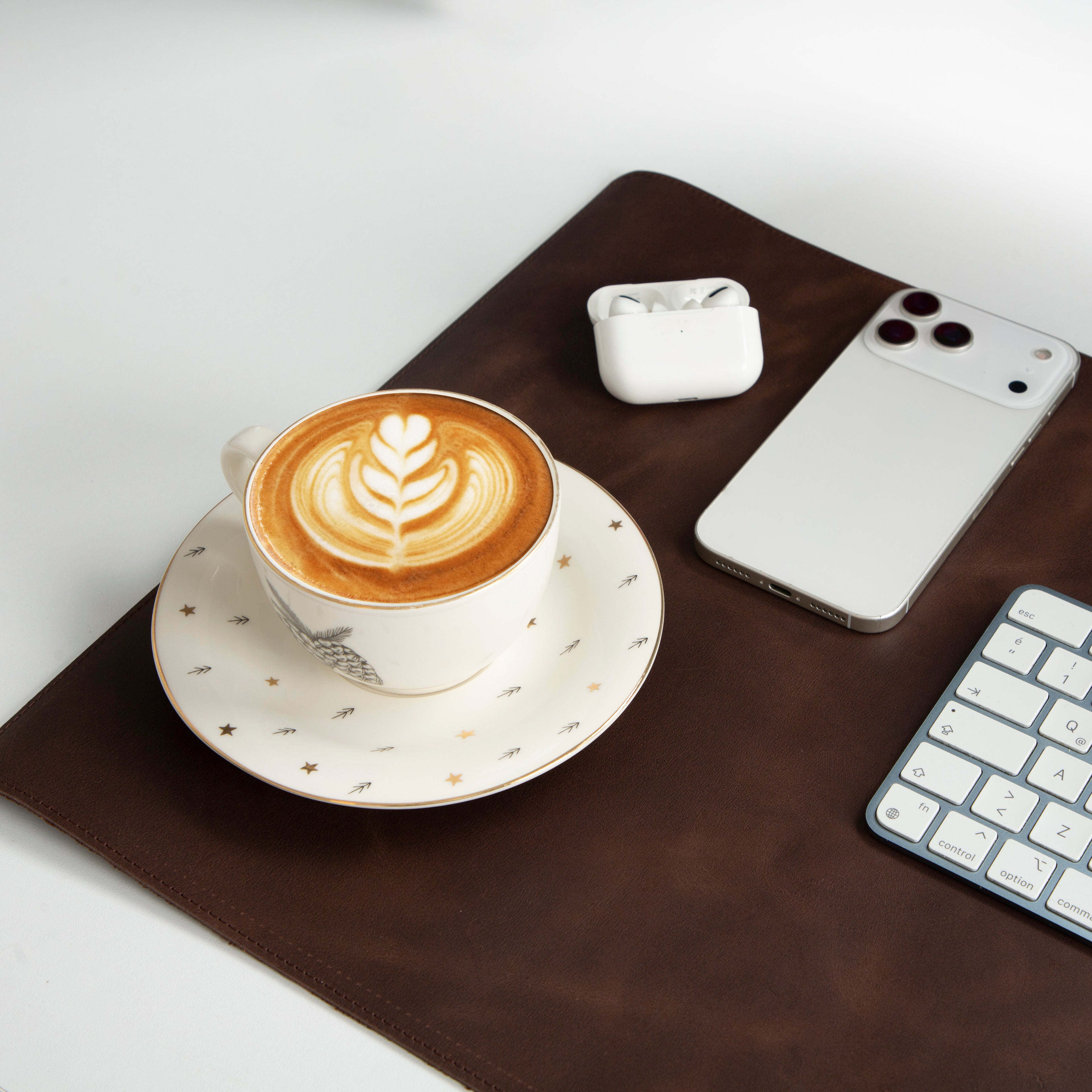 Latte art'lı kahve fincanı, akıllı telefon, kulaklık ve klavye kahverengi mat üzerinde.
