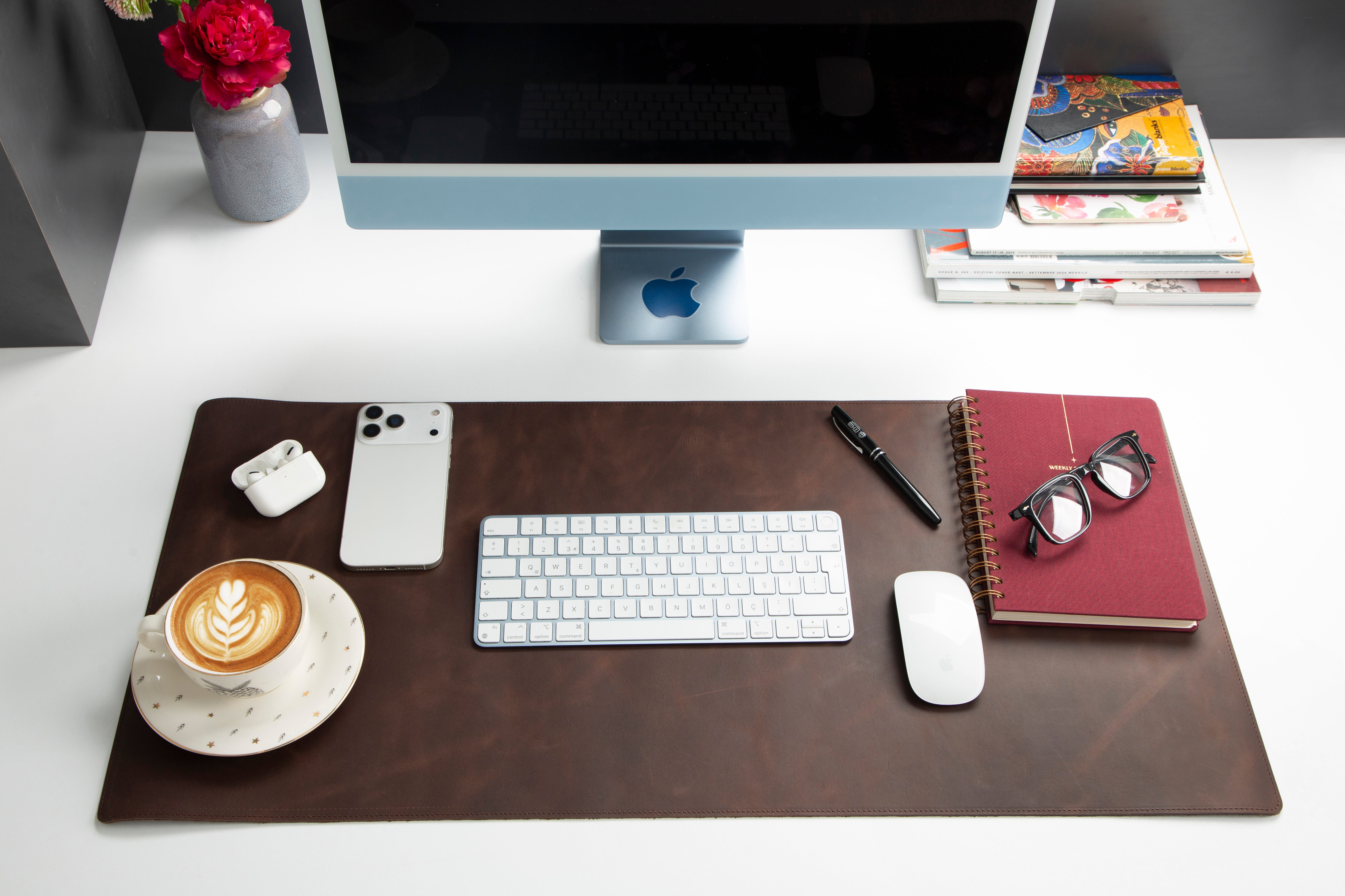 Bir iMac, klavye, fare, telefon, kulaklık, kahve ve defter bulunan bir masa.