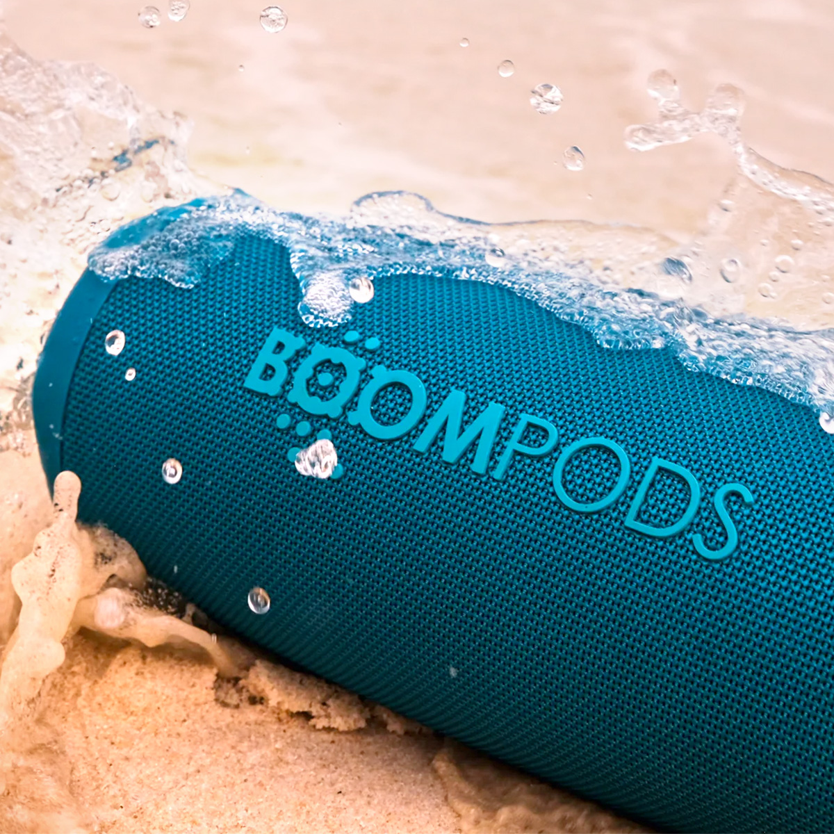 Un altoparlante blu Boompods sulla sabbia schizzato dall'acqua.