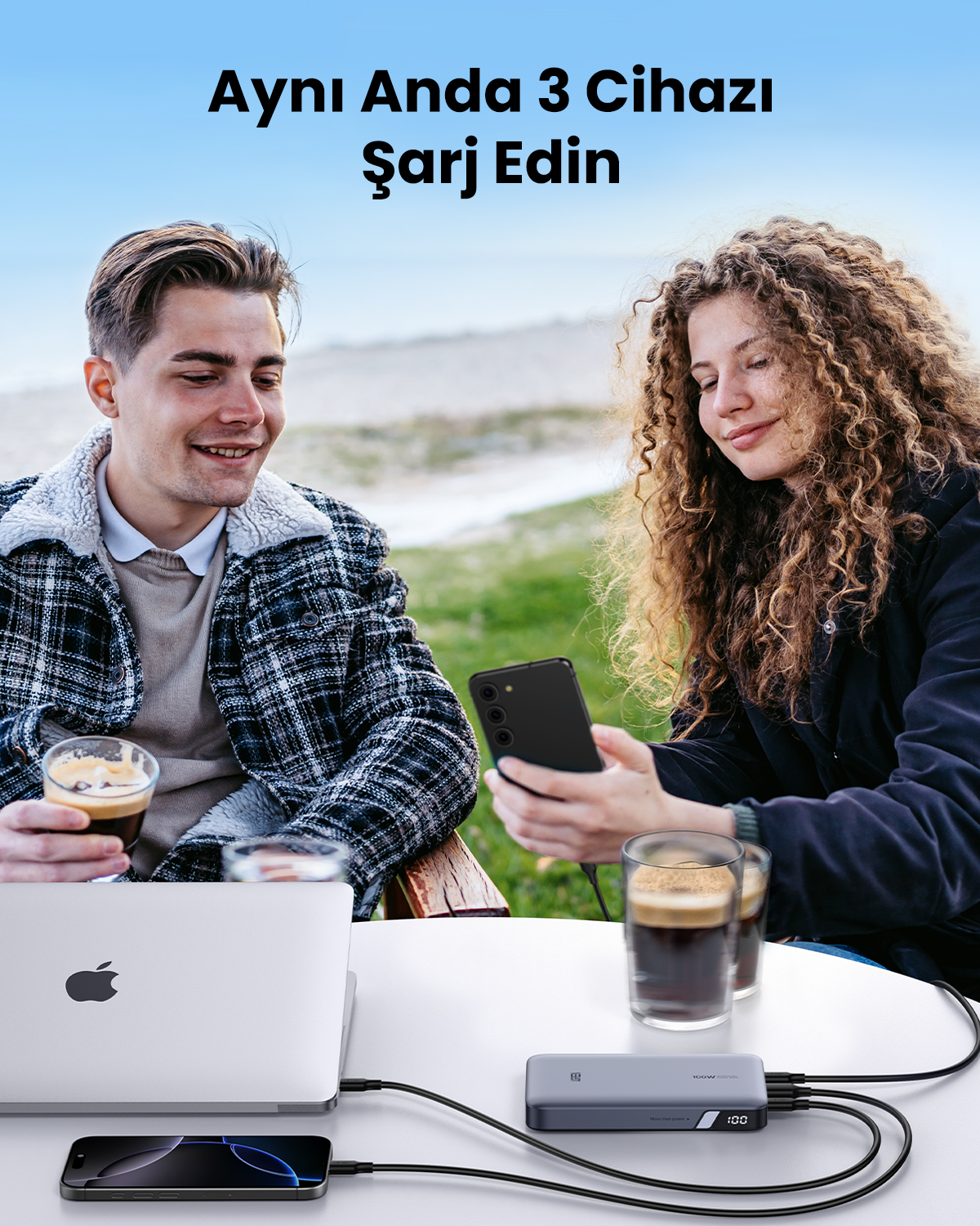 İki kişi dizüstü bilgisayar, iki akıllı telefon ve şarj cihazıyla masada oturuyor.