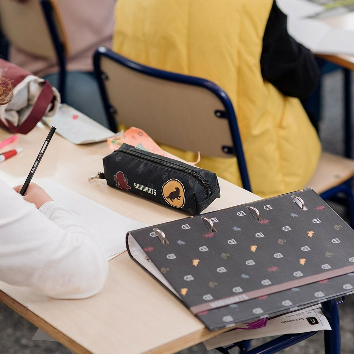 Ein schwarzes Federmäppchen mit Hogwarts-Logo liegt auf einem Schreibtisch neben einem Ordner.