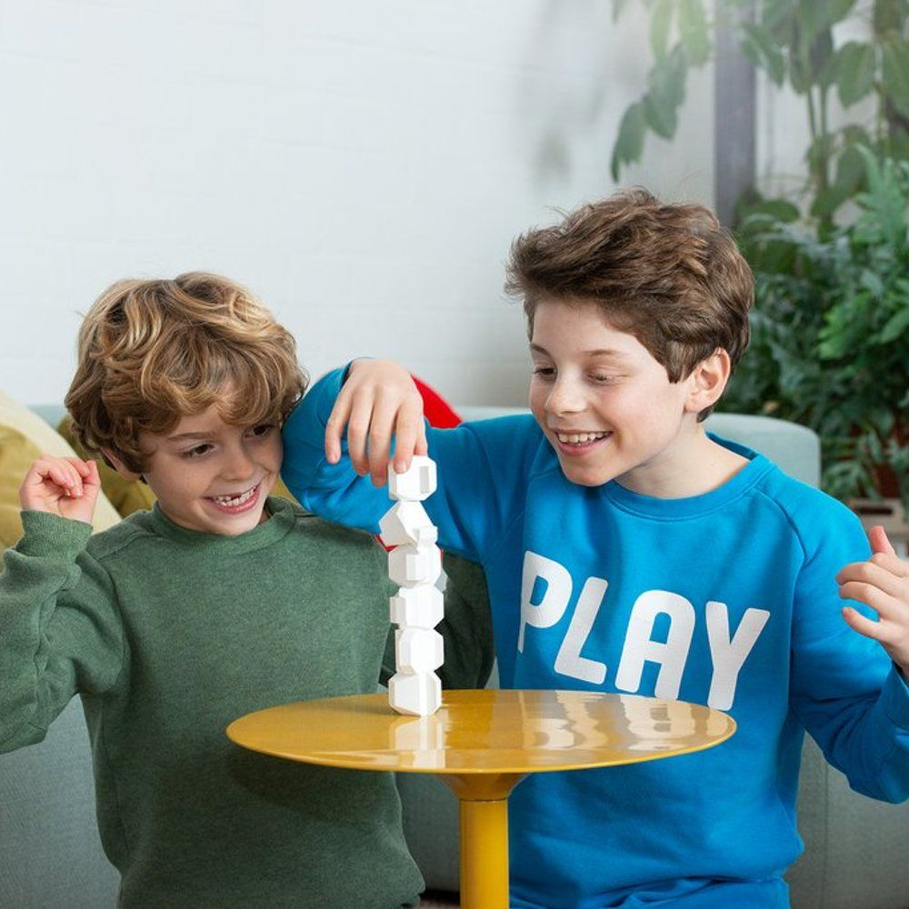 Deux garçons construisent une tour de blocs blancs sur une table jaune.