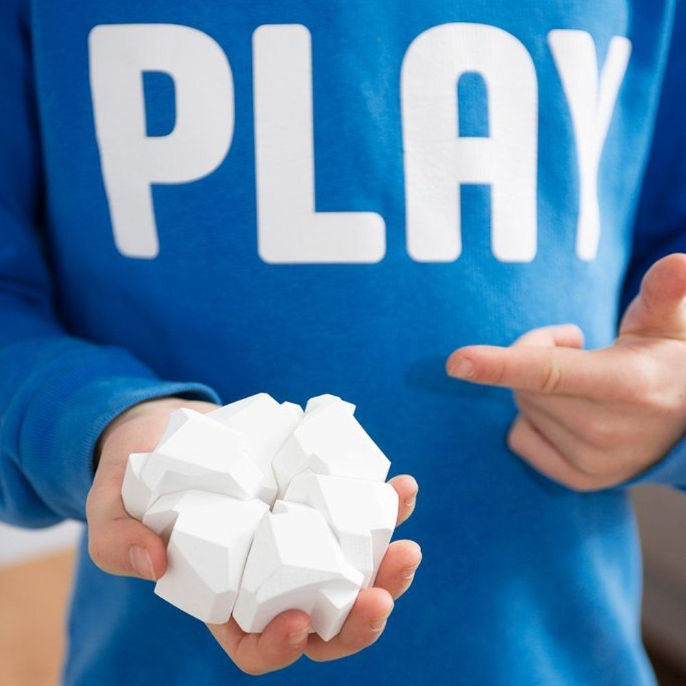 Un enfant tient des blocs géométriques blancs dans sa main, portant un sweat bleu avec le mot PLAY.