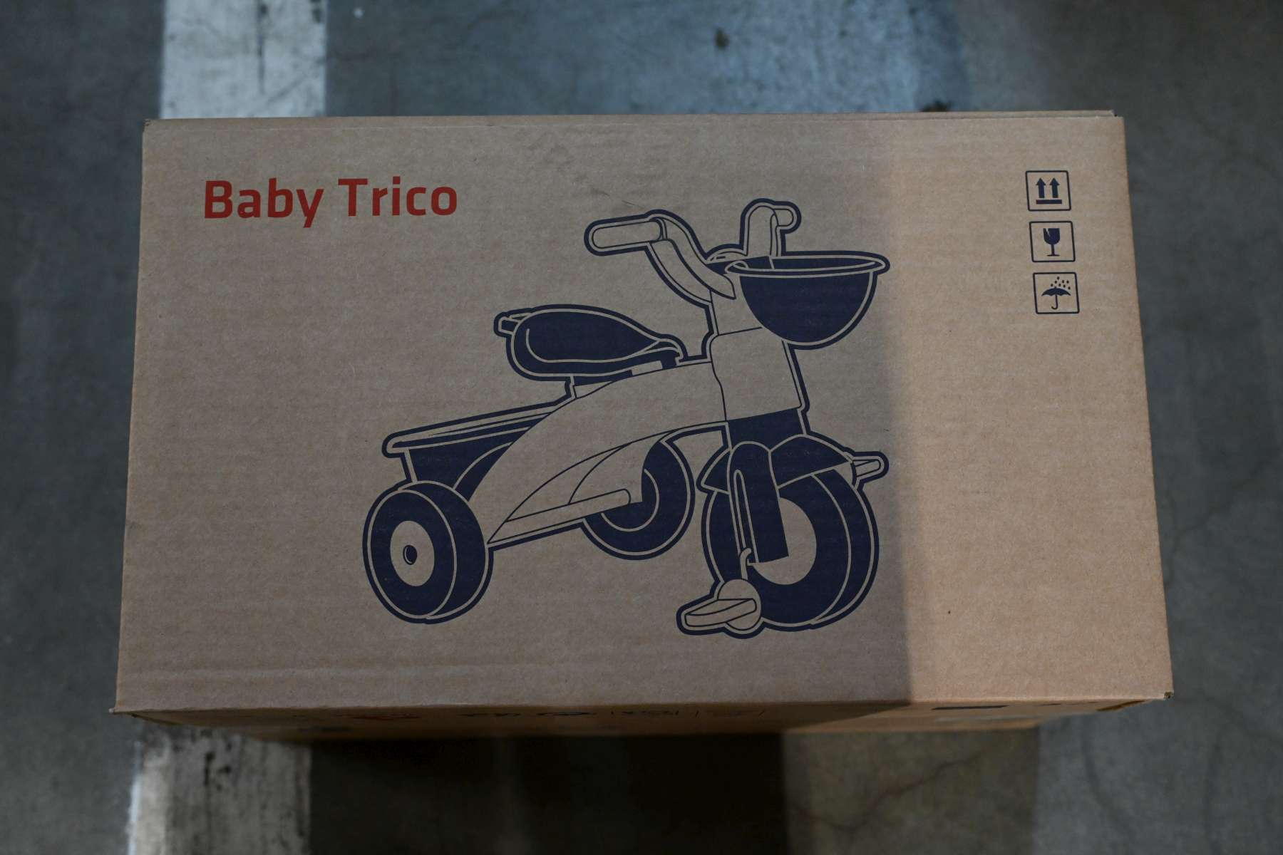 Ein Karton mit der Aufschrift 'Baby Trico' und einer blauen Zeichnung eines Dreirads.