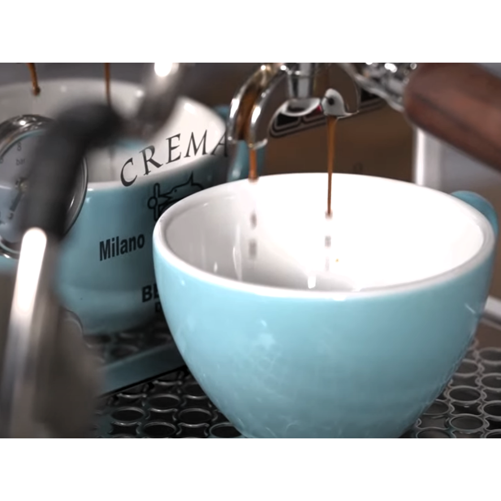 L'espresso coule dans une tasse bleu clair à côté d'une autre tasse étiquetée "CREMA" et "Milano".