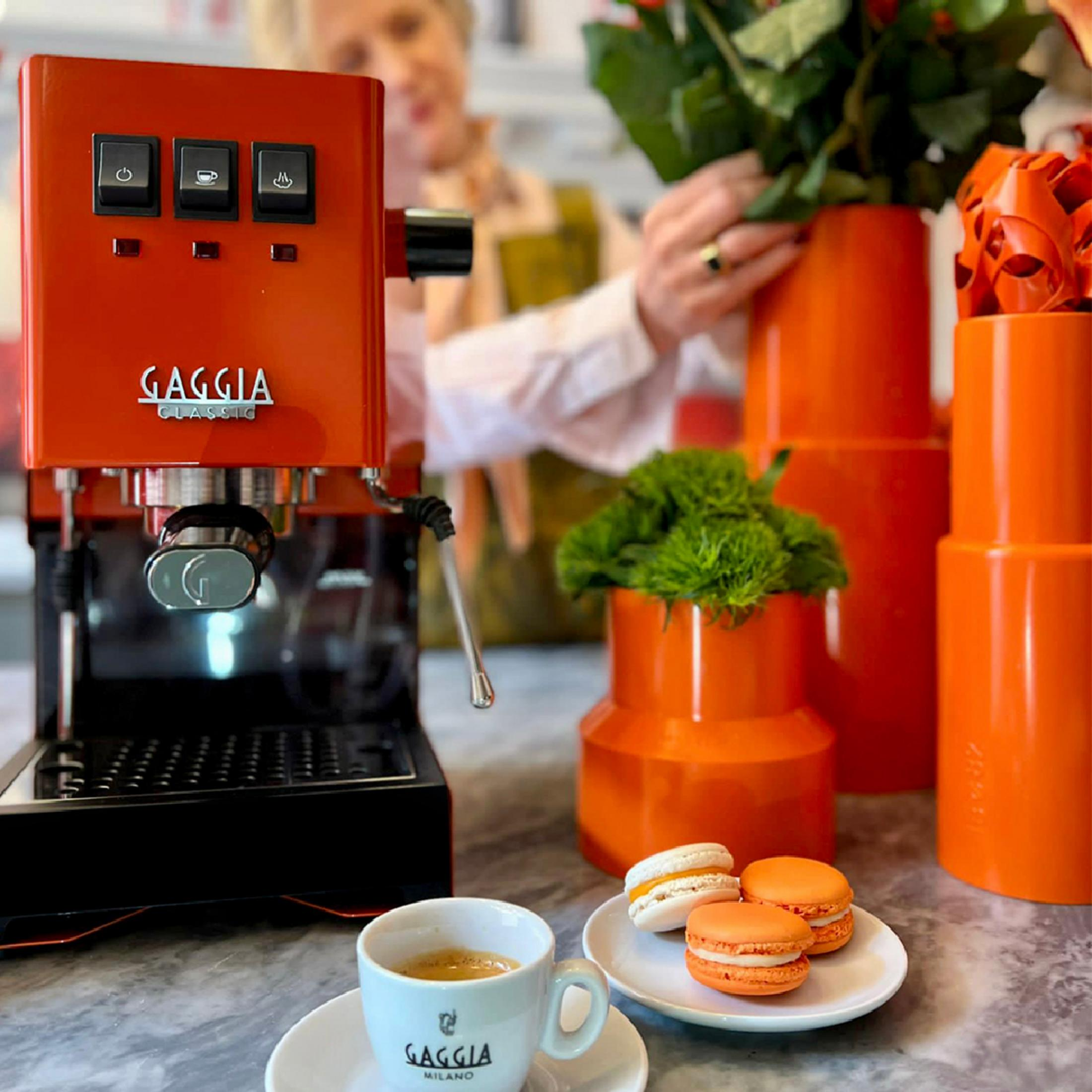 Een oranje espressomachine naast een kop koffie en macarons.