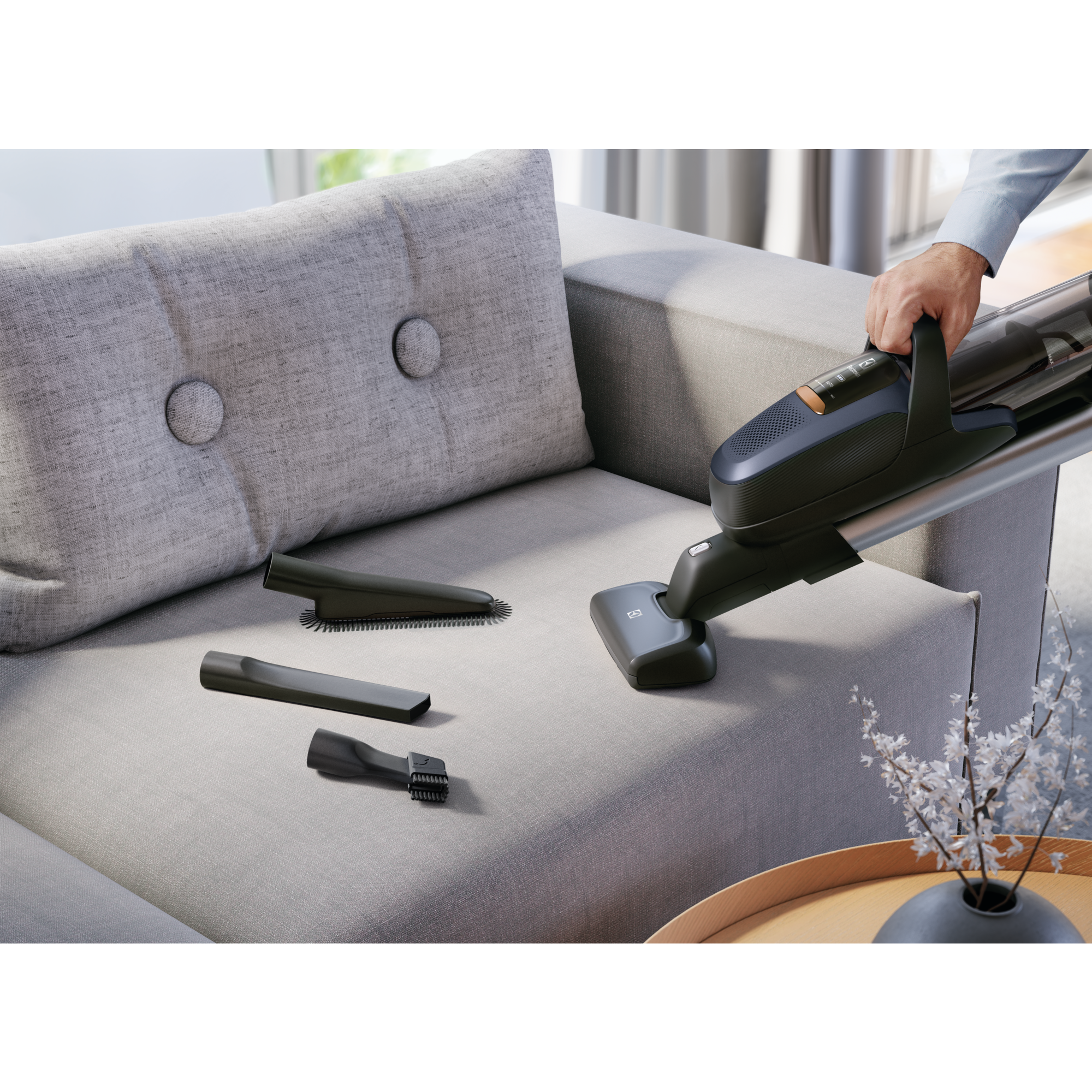 Aspira a mano sofá gris con accesorios. Mesa auxiliar con jarrón al fondo.