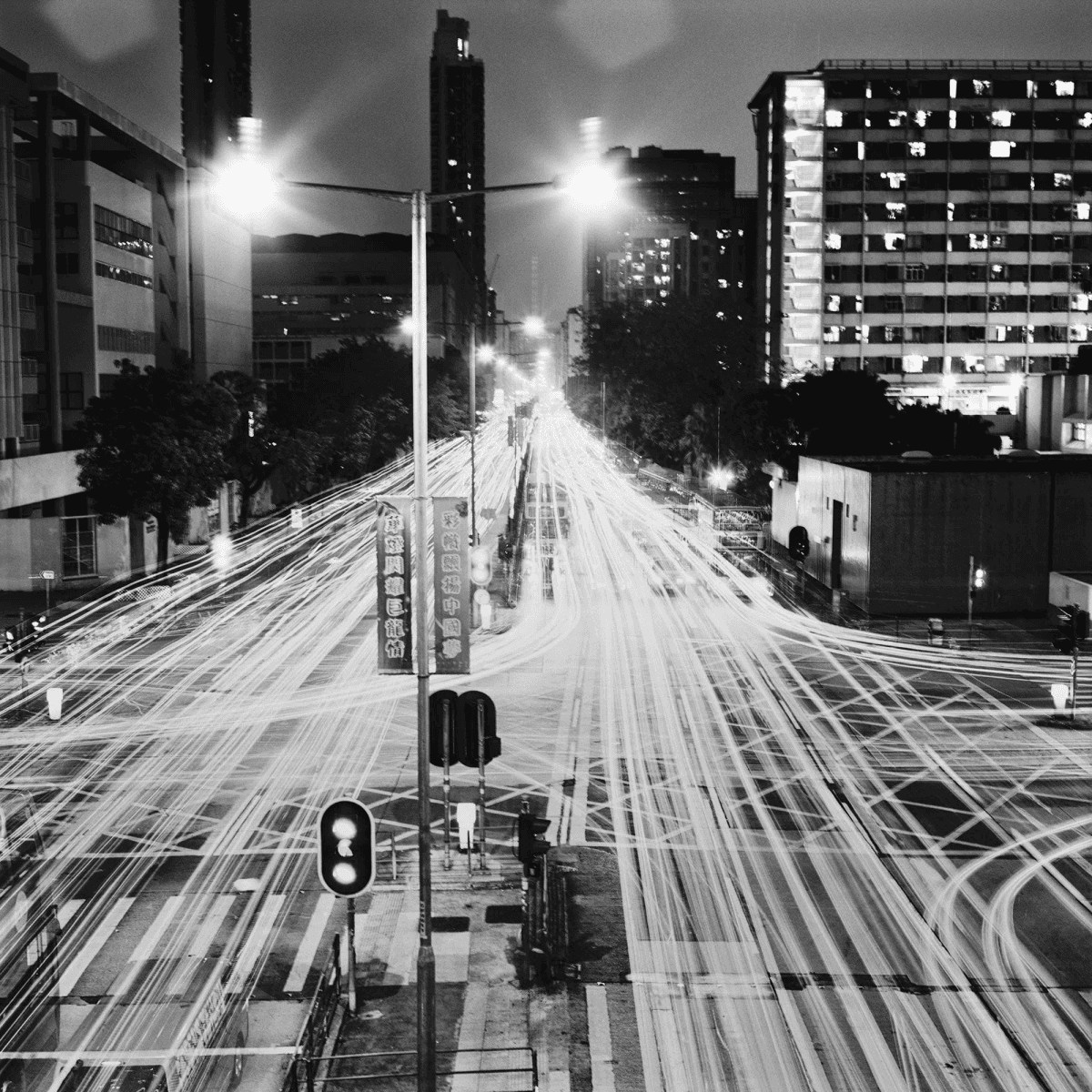 Toma nocturna de una calle concurrida con largas estelas de luz de coches, edificios altos.