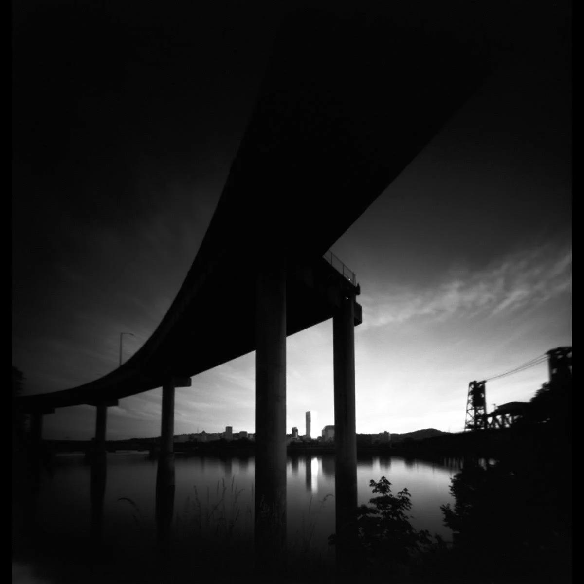Un puente de autopista cruza un río, con un horizonte urbano al fondo.