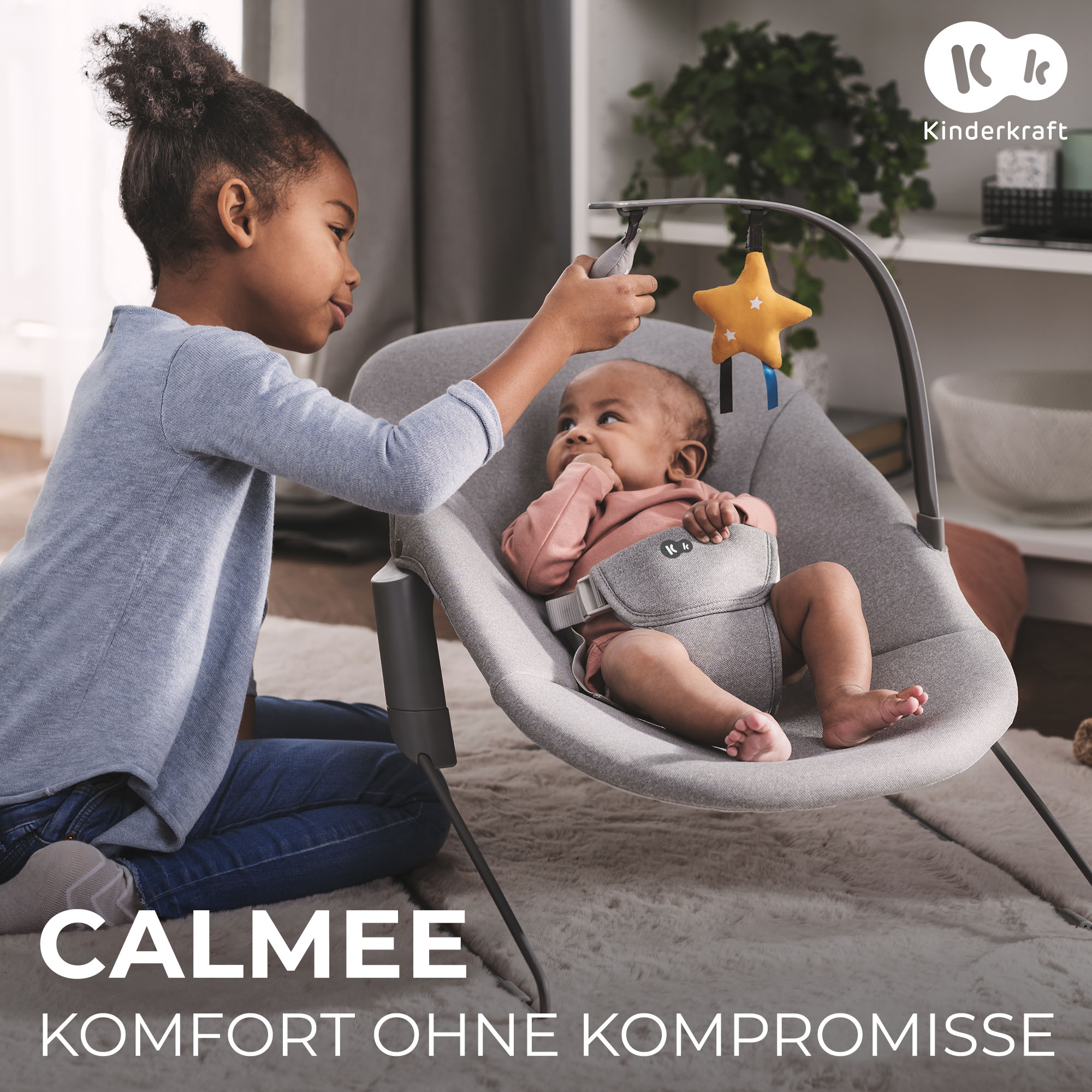 Ein älteres Mädchen spielt mit einem Baby in einer grauen Babyschaukel. Ein Stern hängt über dem Baby.