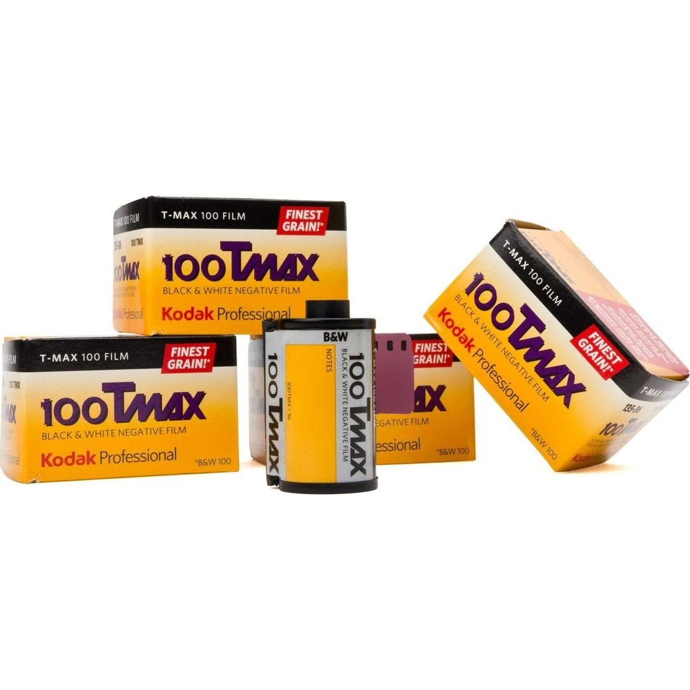 Varios paquetes de película Kodak T-Max 100 y carretes de película dispuestos sobre fondo blanco.