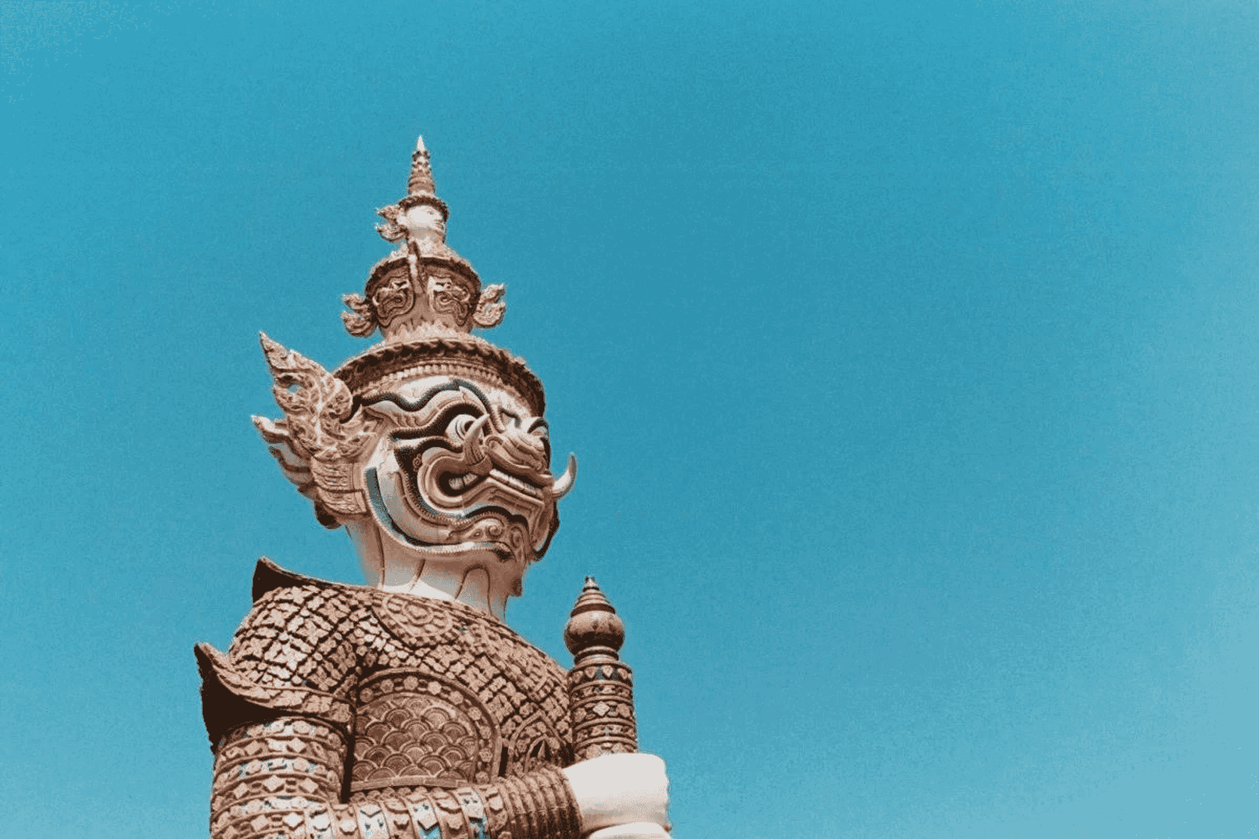 Una estatua de piedra de un guerrero mCtico con armadura ornamentada y rostro fiero contra cielo azul.
