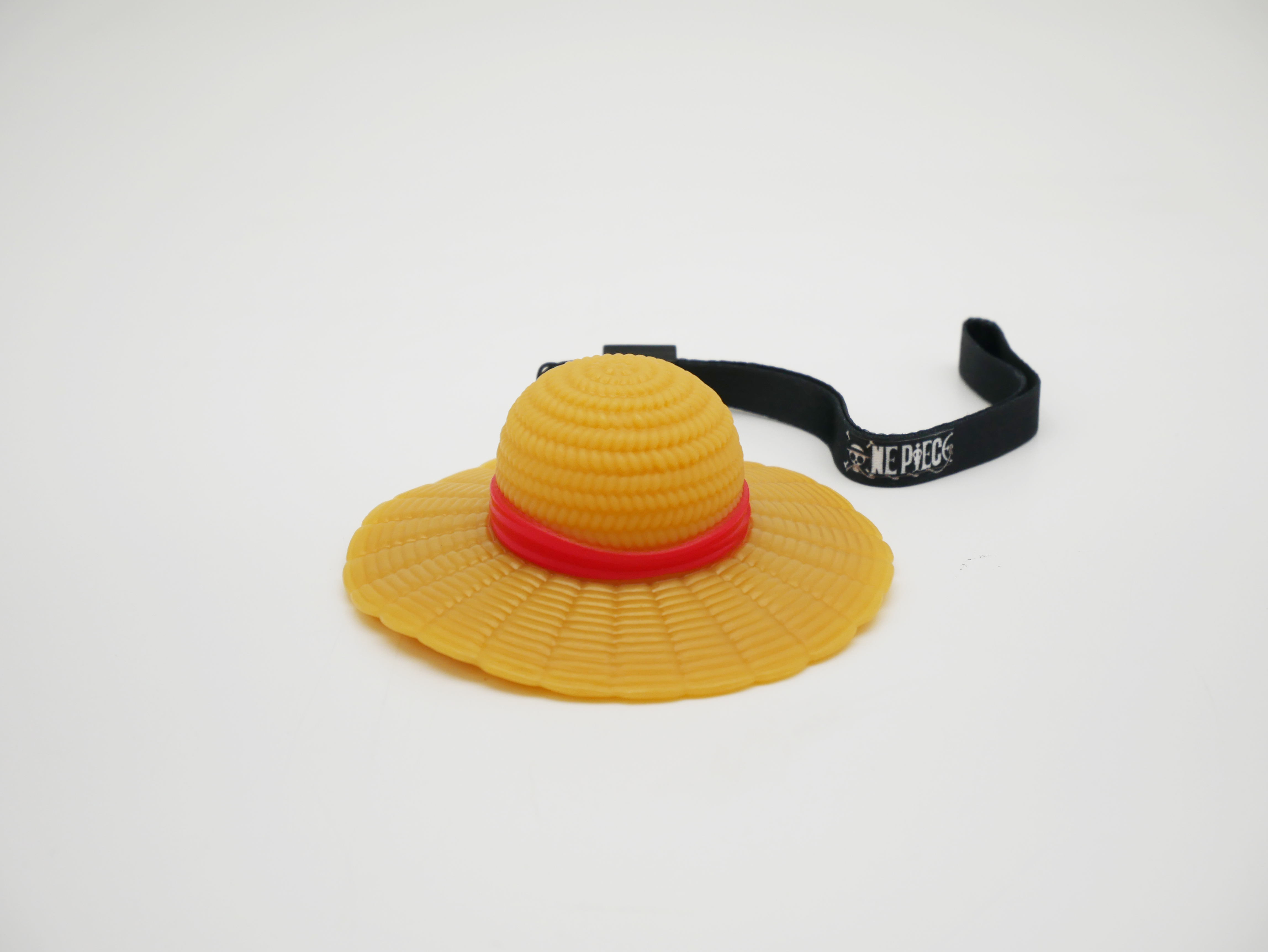 Un chapeau jaune avec une bande rouge et une sangle noire "ONE PIECE".