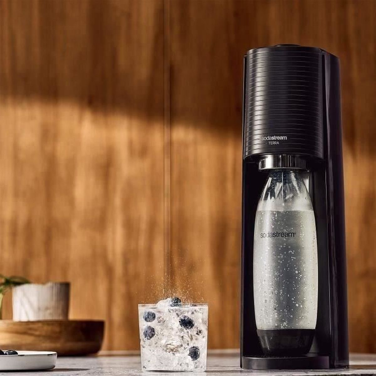 Czarny SodaStream Terra z szklaną butelką i szklanką z lodem i borówkami.