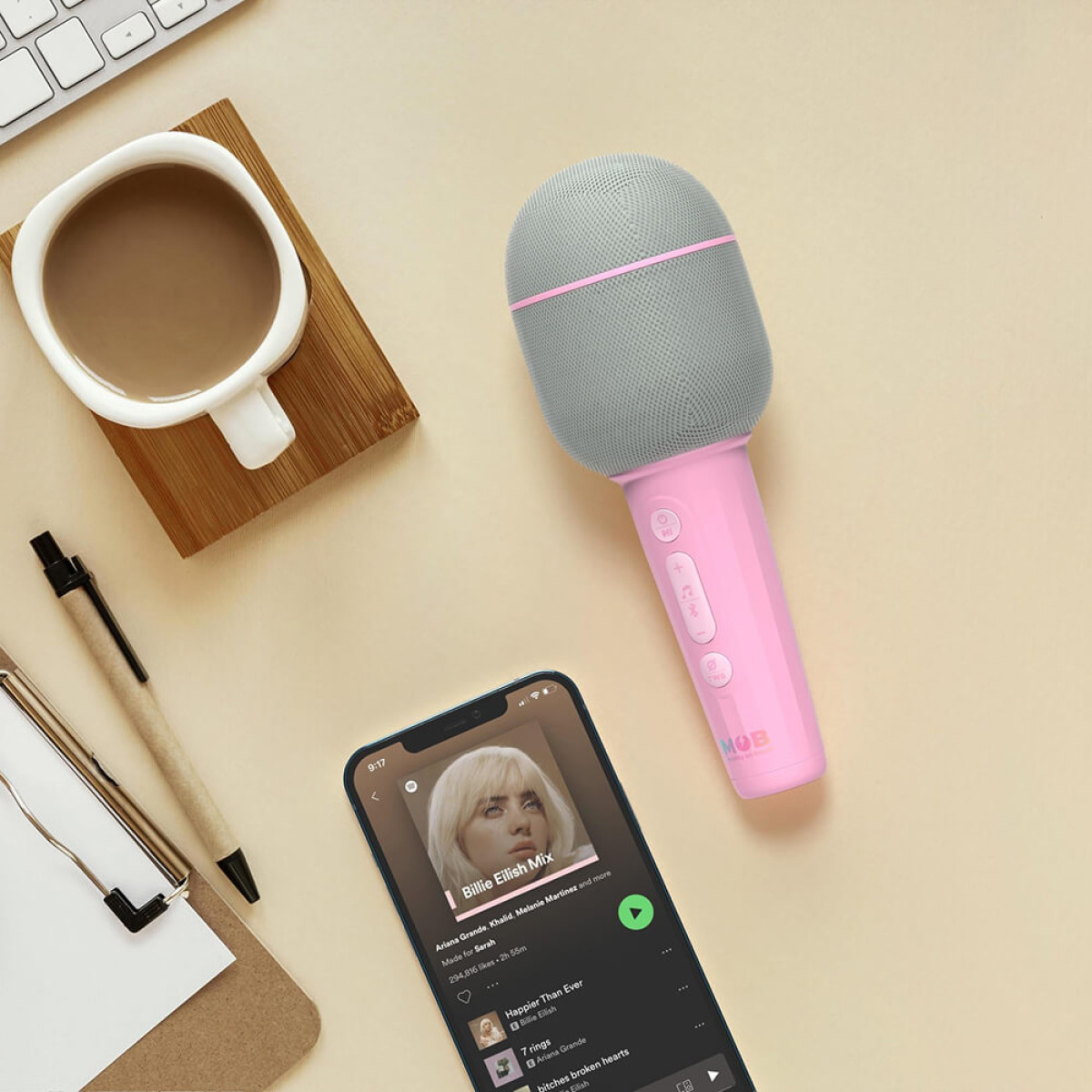 Un microfono rosa accanto a una tazza di caffè e uno smartphone che riproduce musica.