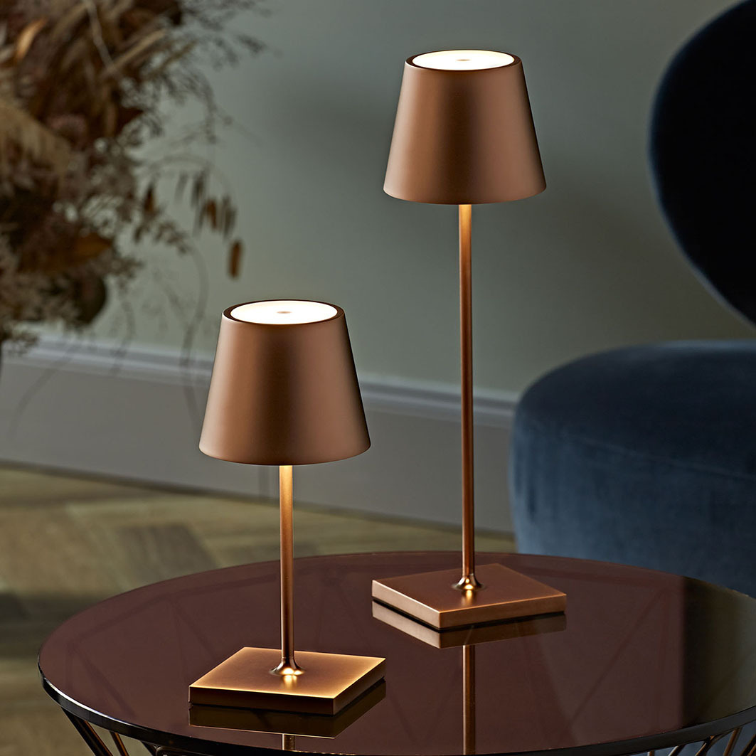 Zwei kupferfarbene Tischlampen mit kegelförmigen Schirmen stehen auf einem runden Tisch.