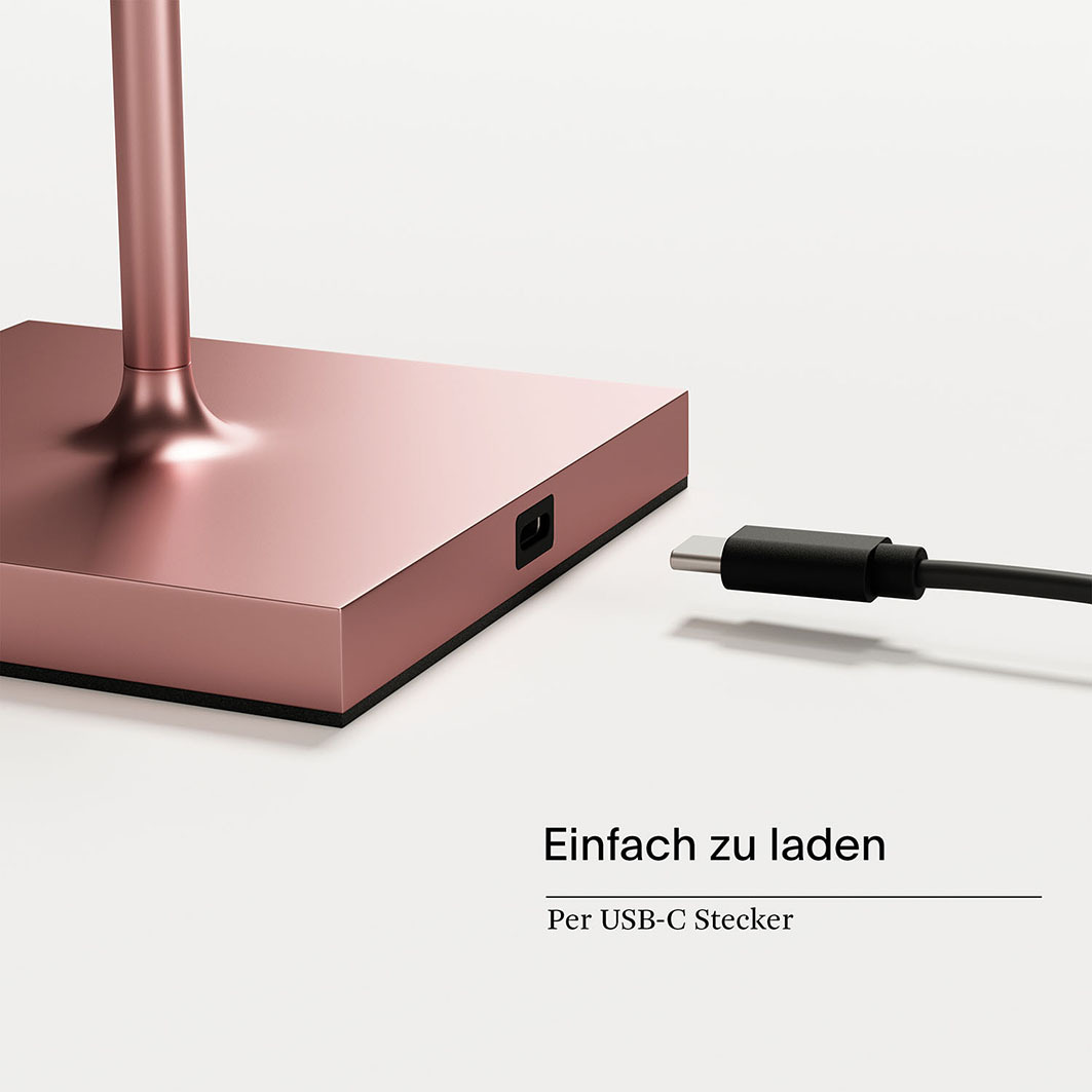 Ein rosafarbenes Ladekabel wird in eine rechteckige Buchse an der Basis einer Lampe gesteckt.