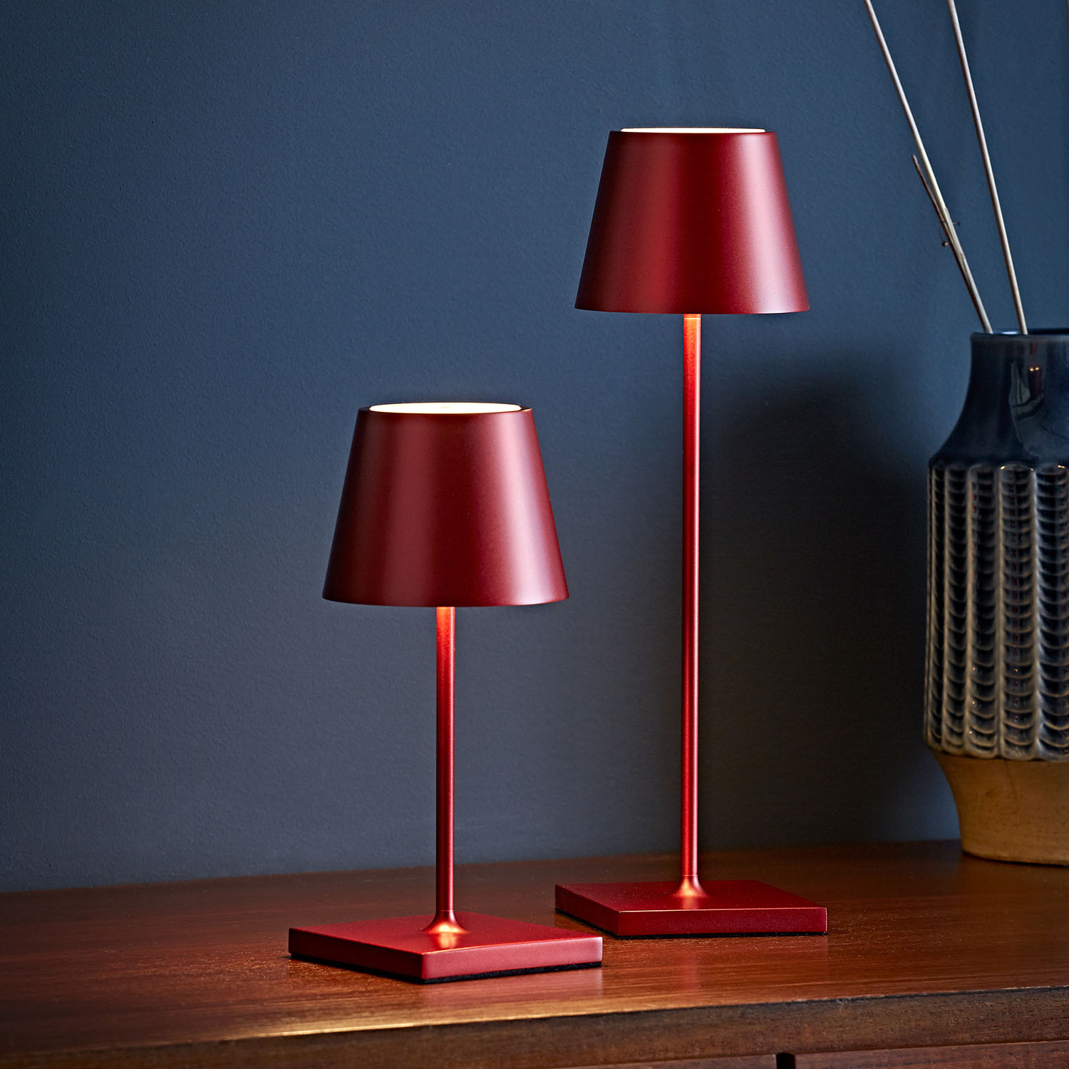 Zwei rote Tischlampen stehen auf einem Holztisch vor einer blauen Wand.