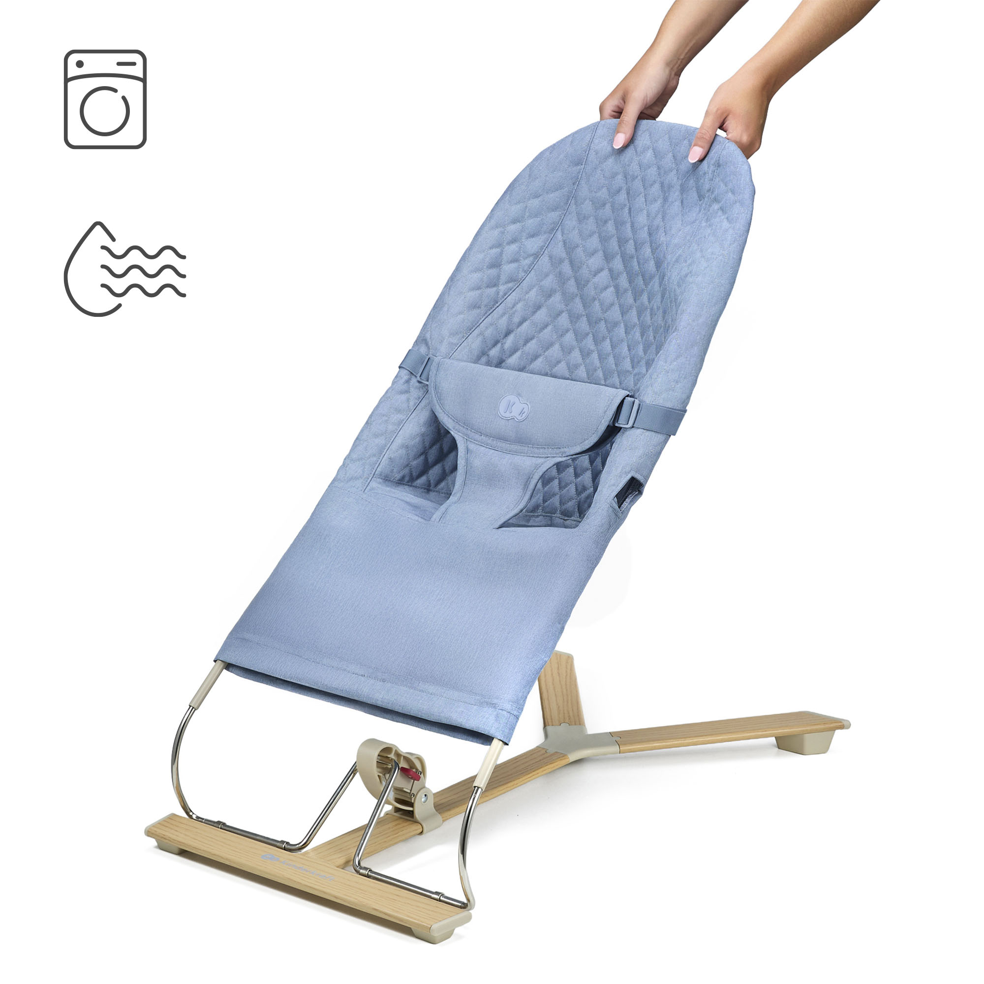 Eine blaue Babywippe mit Holzrahmen, von Händen gehalten. Wasch- und Trocknersymbole.