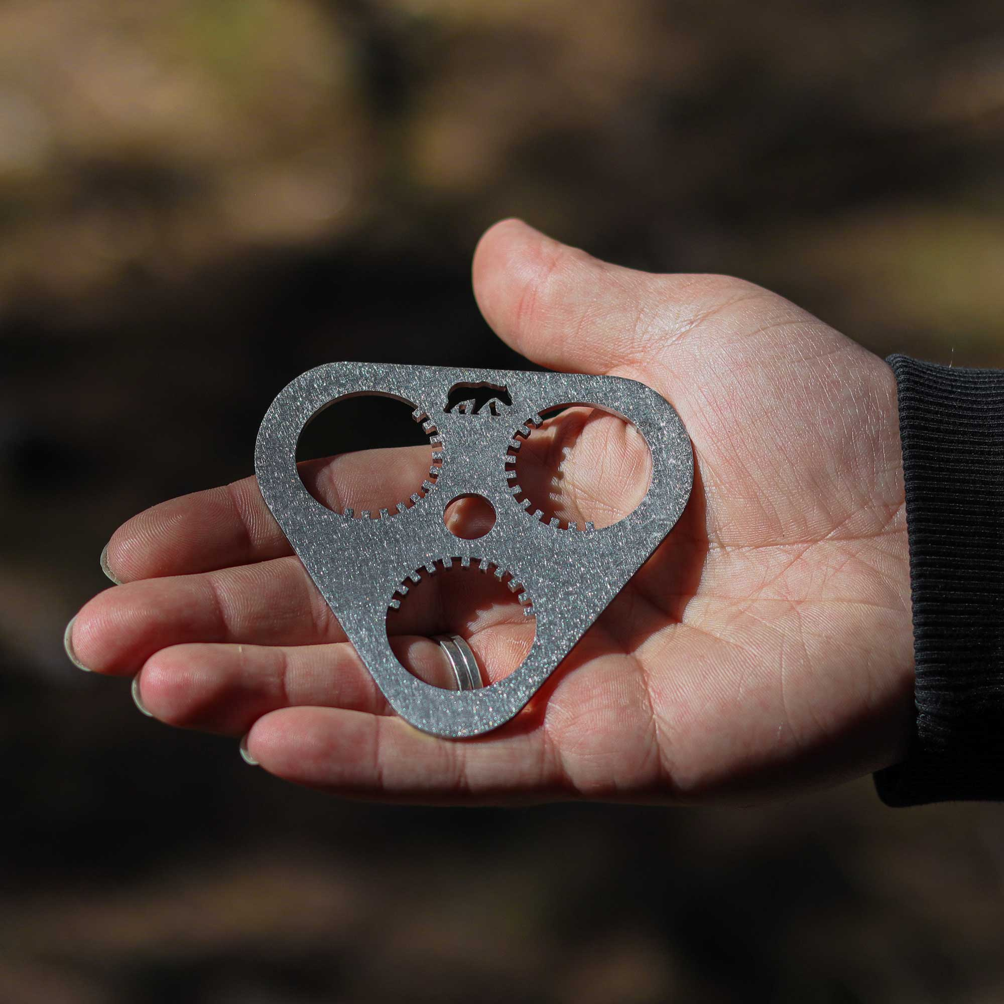 Bir el, üç dairesel kesiği ve bir ayı silüeti olan gri üçgen bir alet tutuyor.
