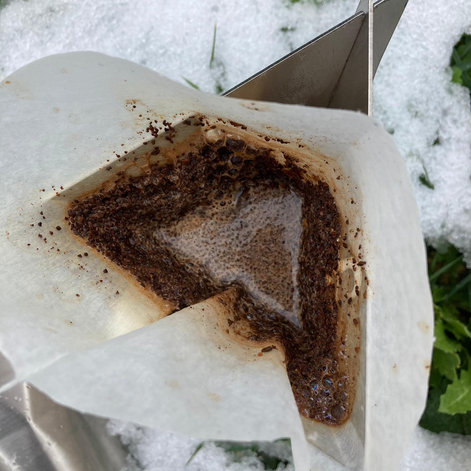 Kahve telvesi ve suyu olan bir kahve filtresi karın üzerinde duruyor.