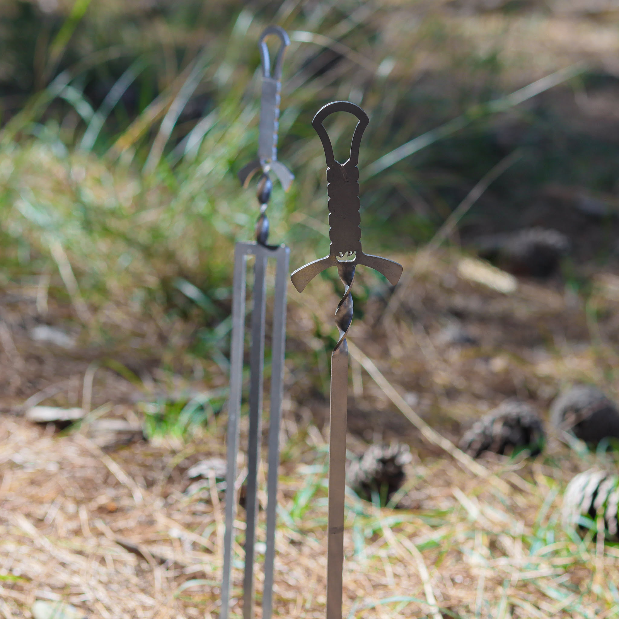 Kılıç kabzası tasarımlı iki metal şiş çimlerin üzerinde duruyor.