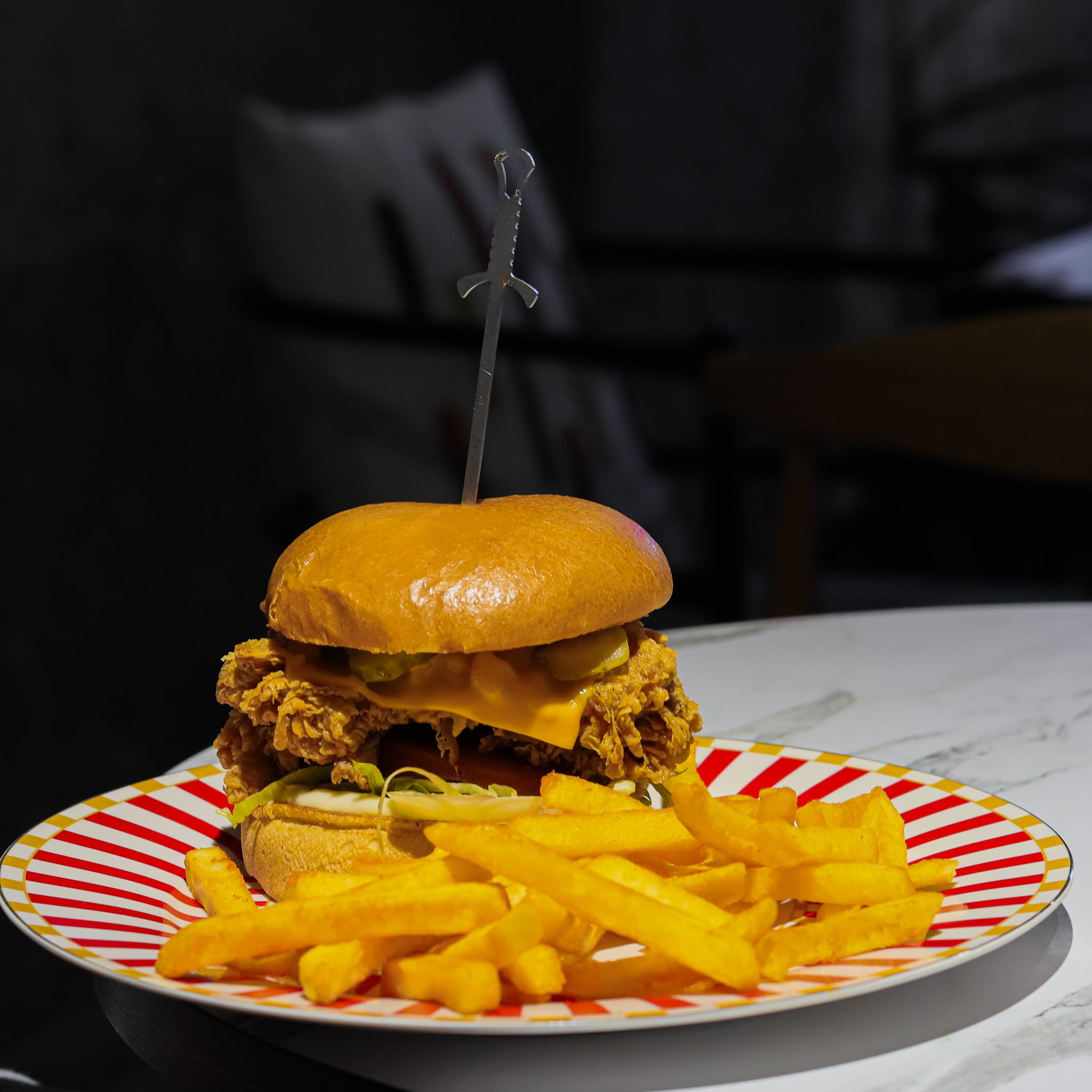 Peynirli ve turşulu tavuklu burger, kırmızı beyaz tabakta patates kızartması ile servis edilir.