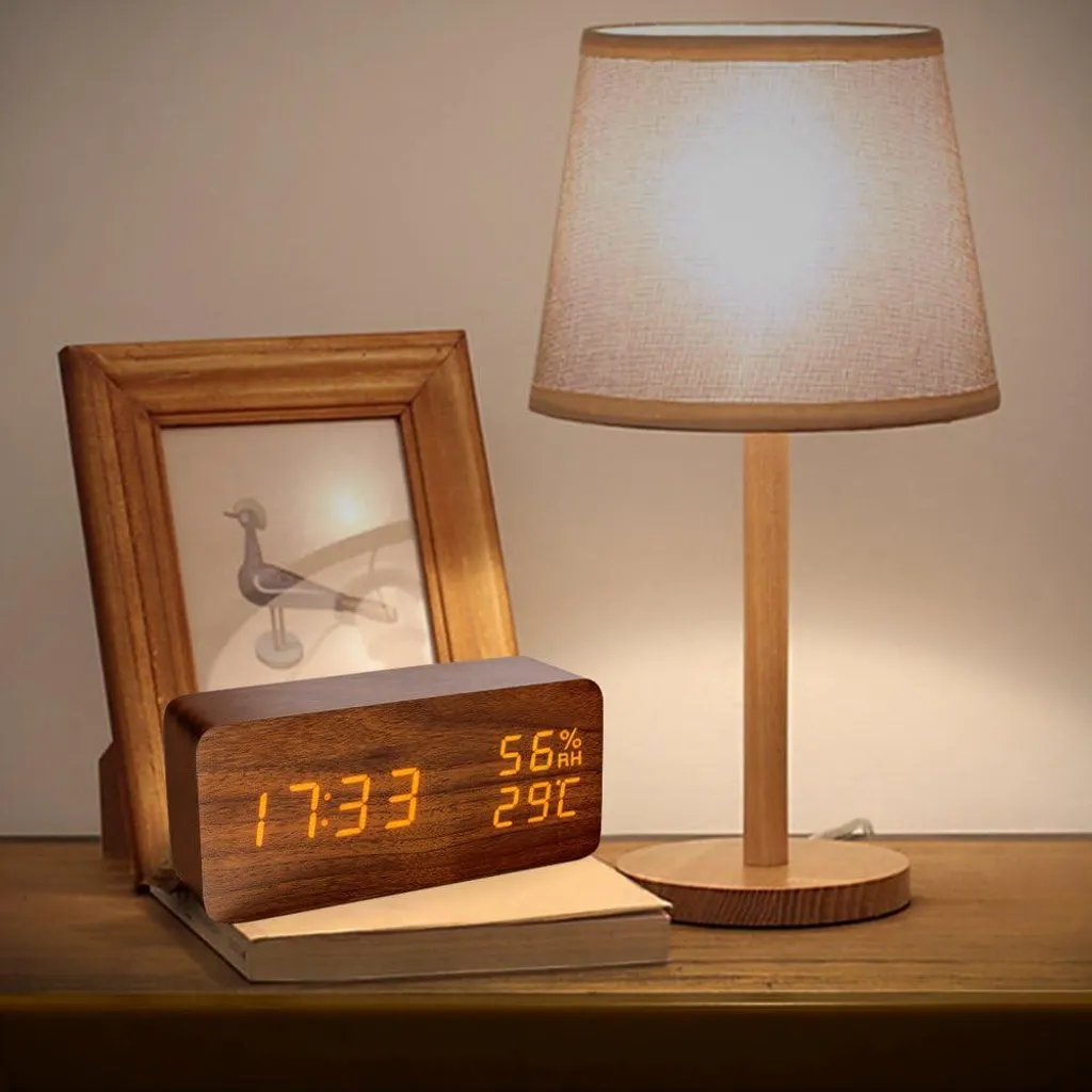 Holzwecker mit digitaler Anzeige, daneben ein Bilderrahmen und eine Lampe.