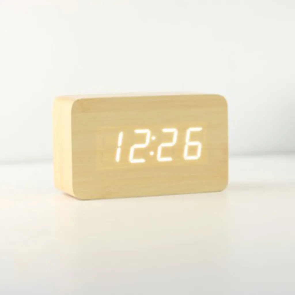 Ein hölzerner Digitalwecker zeigt 12:26 auf einem weißen Tisch.