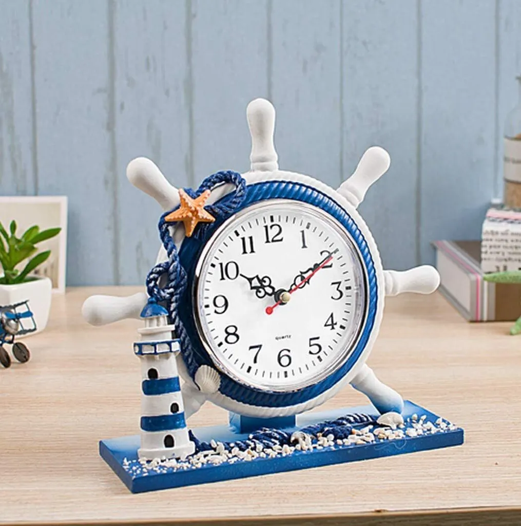 Ein Schiffsrad-Wecker mit Leuchtturm, Seestern und Muscheln auf blauem Sockel.