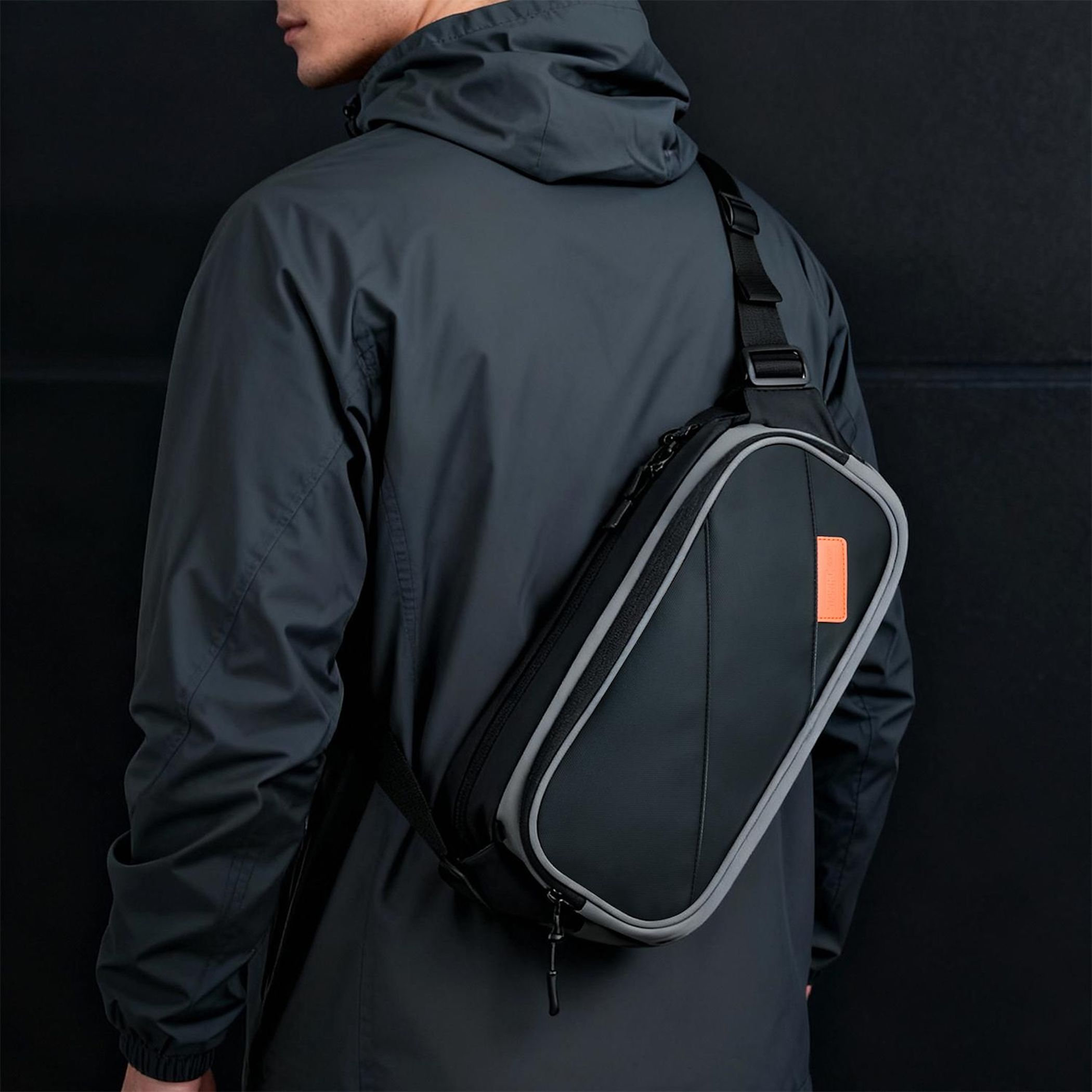 Mann mit Umhängetasche in Grau und Schwarz mit orangefarbener Lasche.