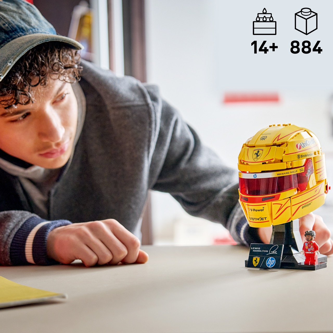 Çocuk stanttaki çıkartmalı ve figürlü sarı LEGO kaskına bakıyor.