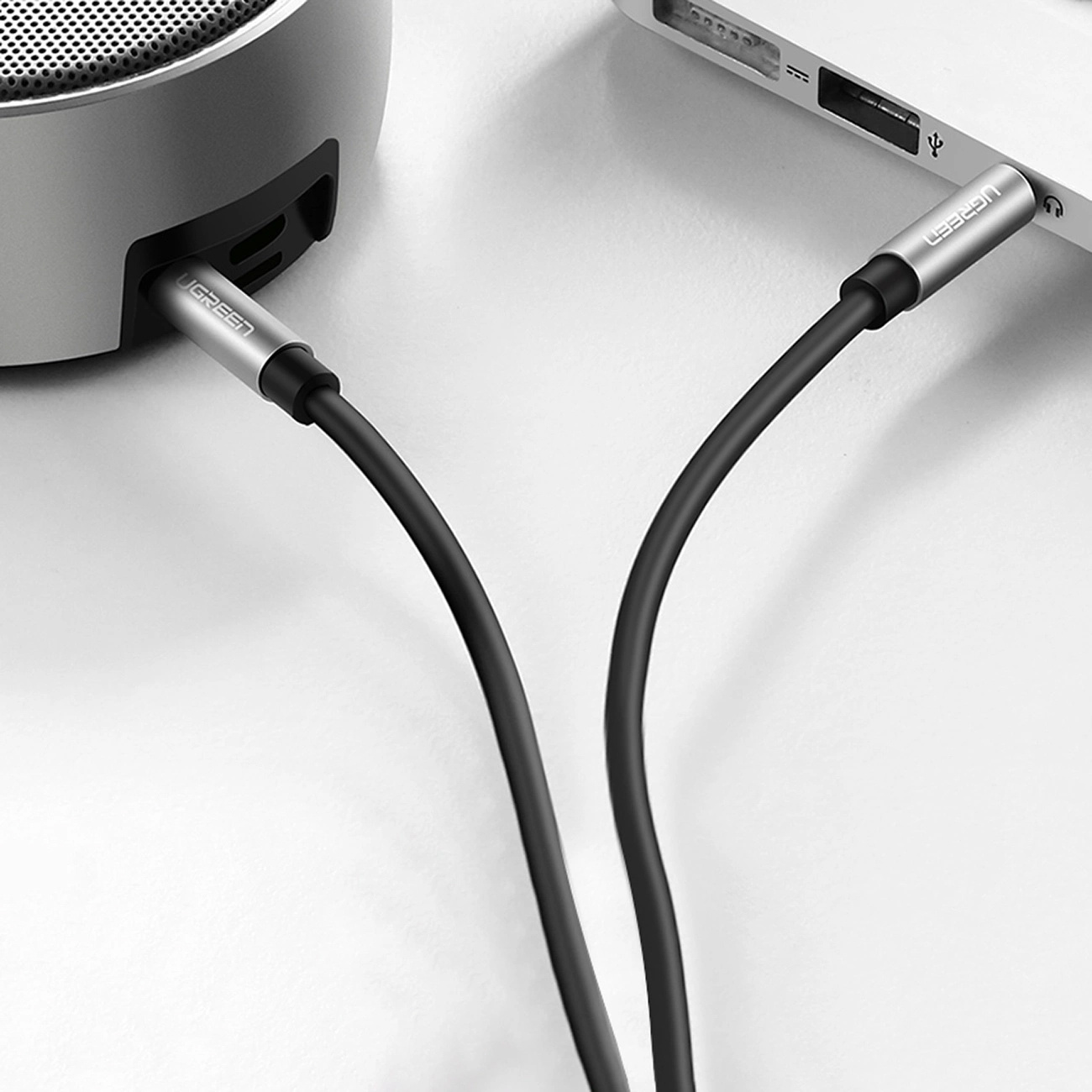 Ein schwarzes Audiokabel verbindet einen silbernen Lautsprecher mit einem Laptop.