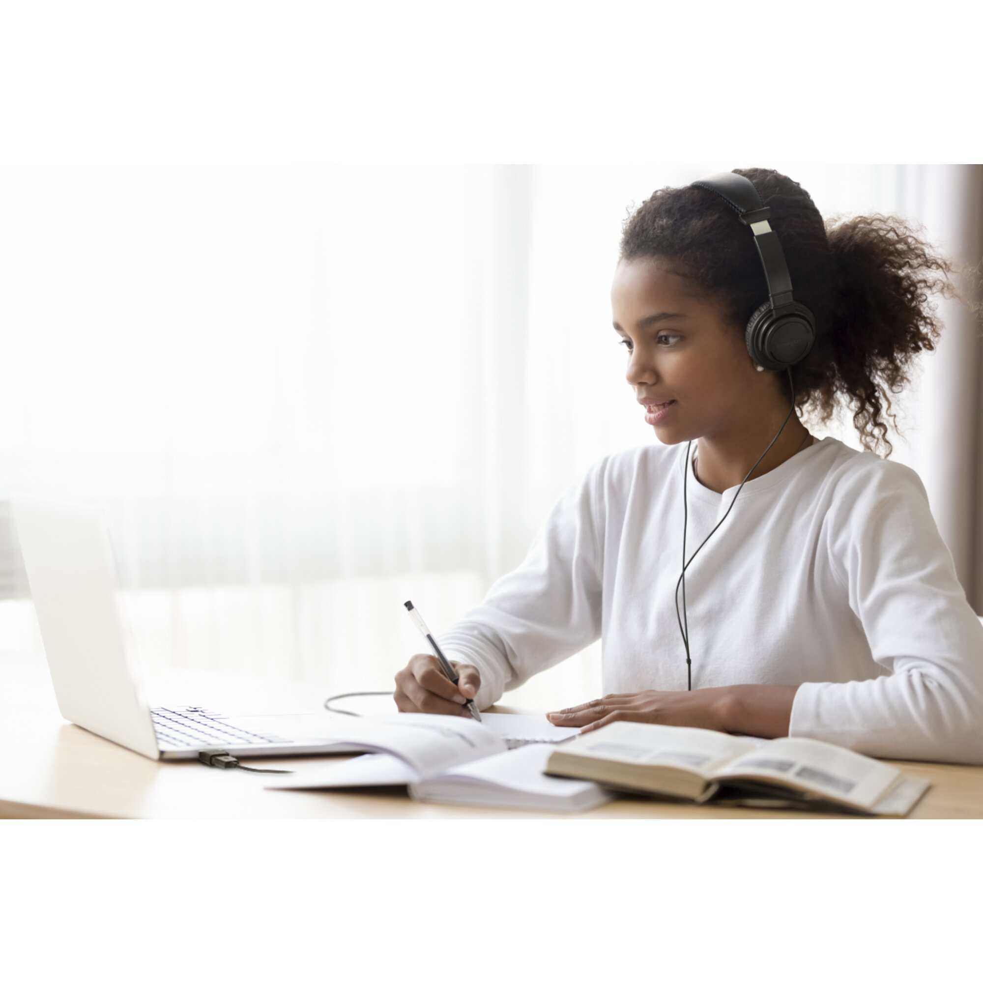 Une jeune fille avec un casque écrit dans un carnet en regardant un ordinateur portable.