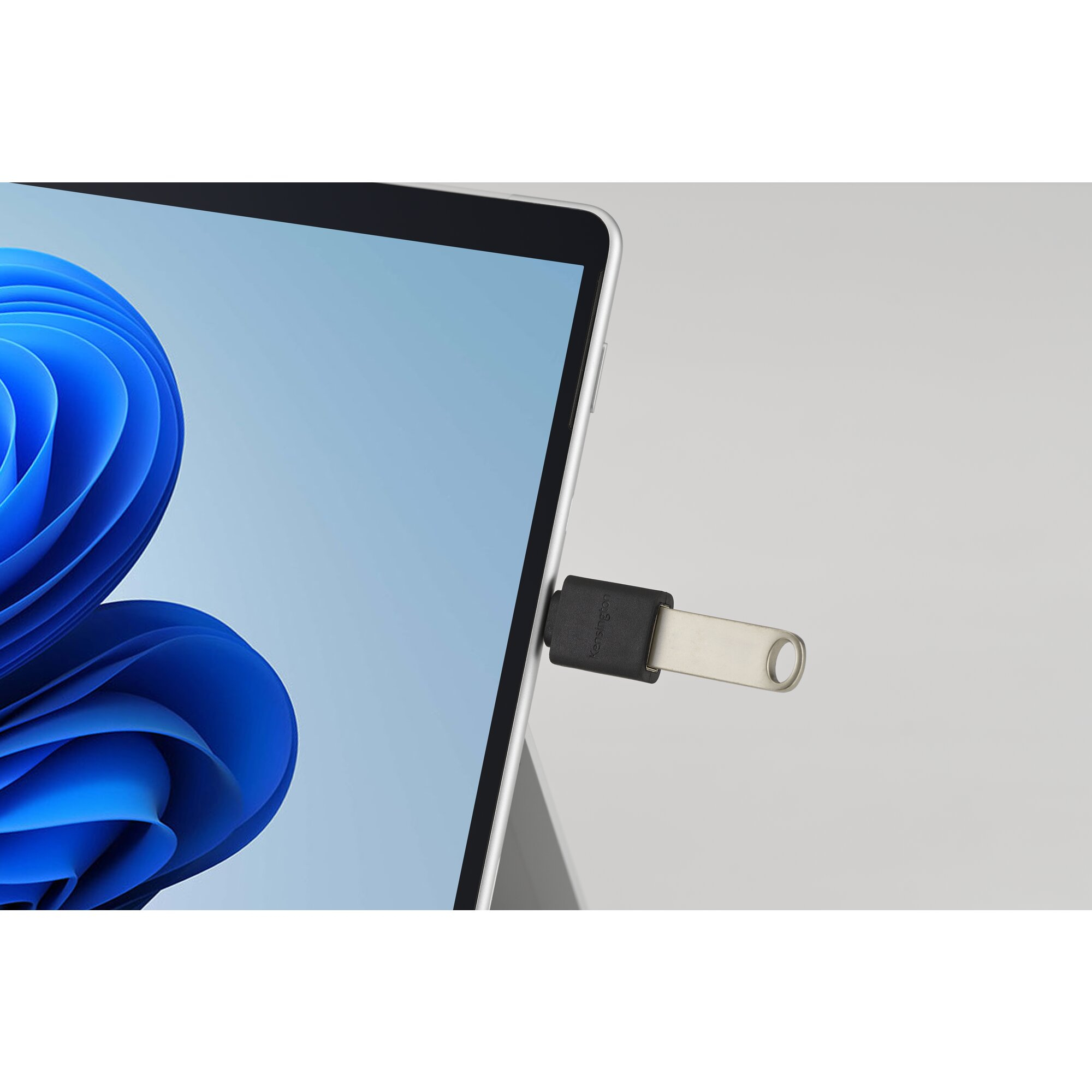 Une clé USB est branchée sur une tablette, sur un fond gris clair.