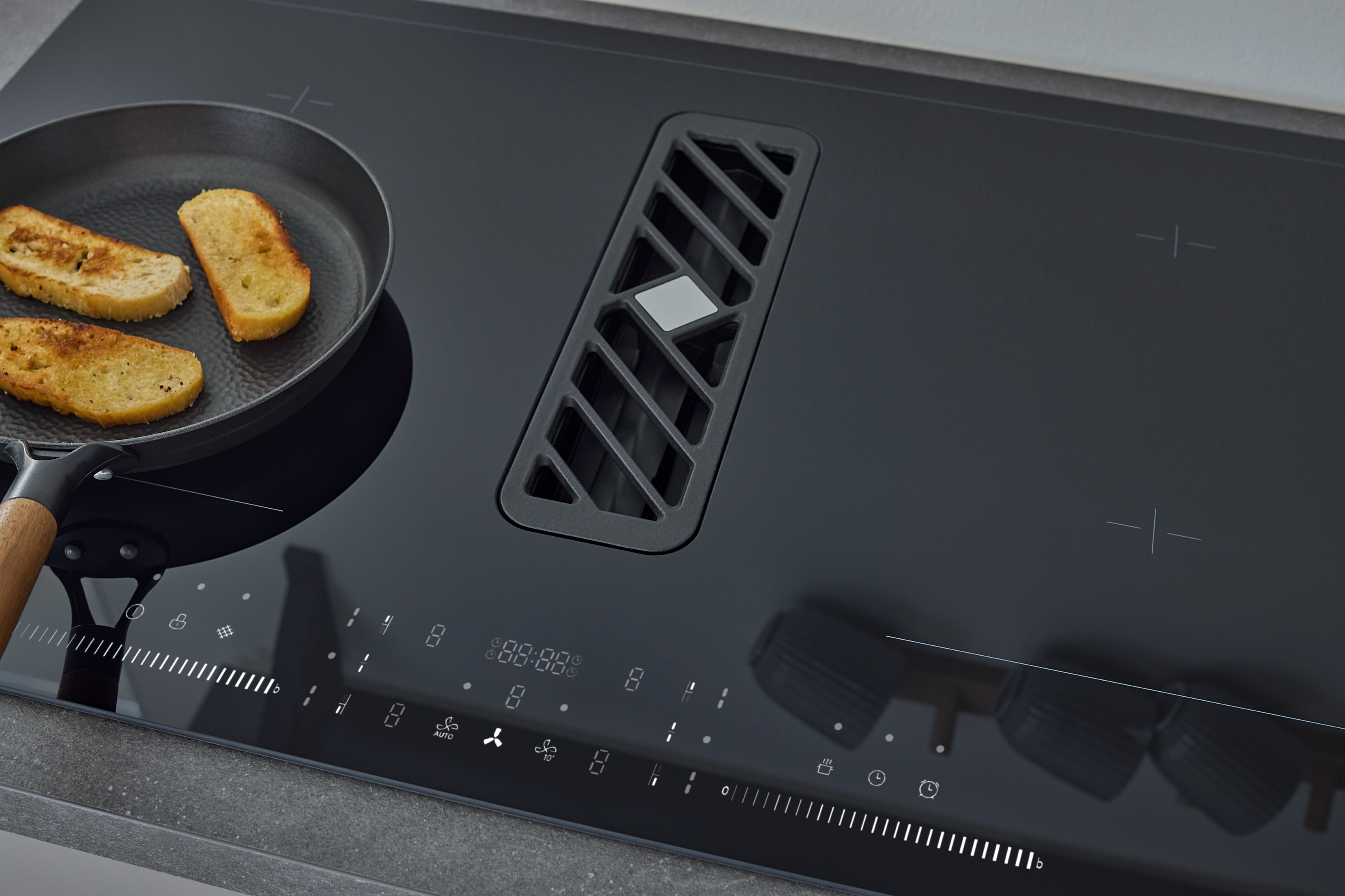 Des toasts grillent dans une poêle sur une plaque à induction noire avec hotte intégrée.