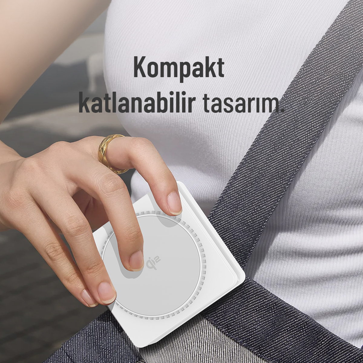 Bir el, omuz askısı üzerinde duran beyaz, yuvarlak bir Qi şarj cihazı tutuyor.